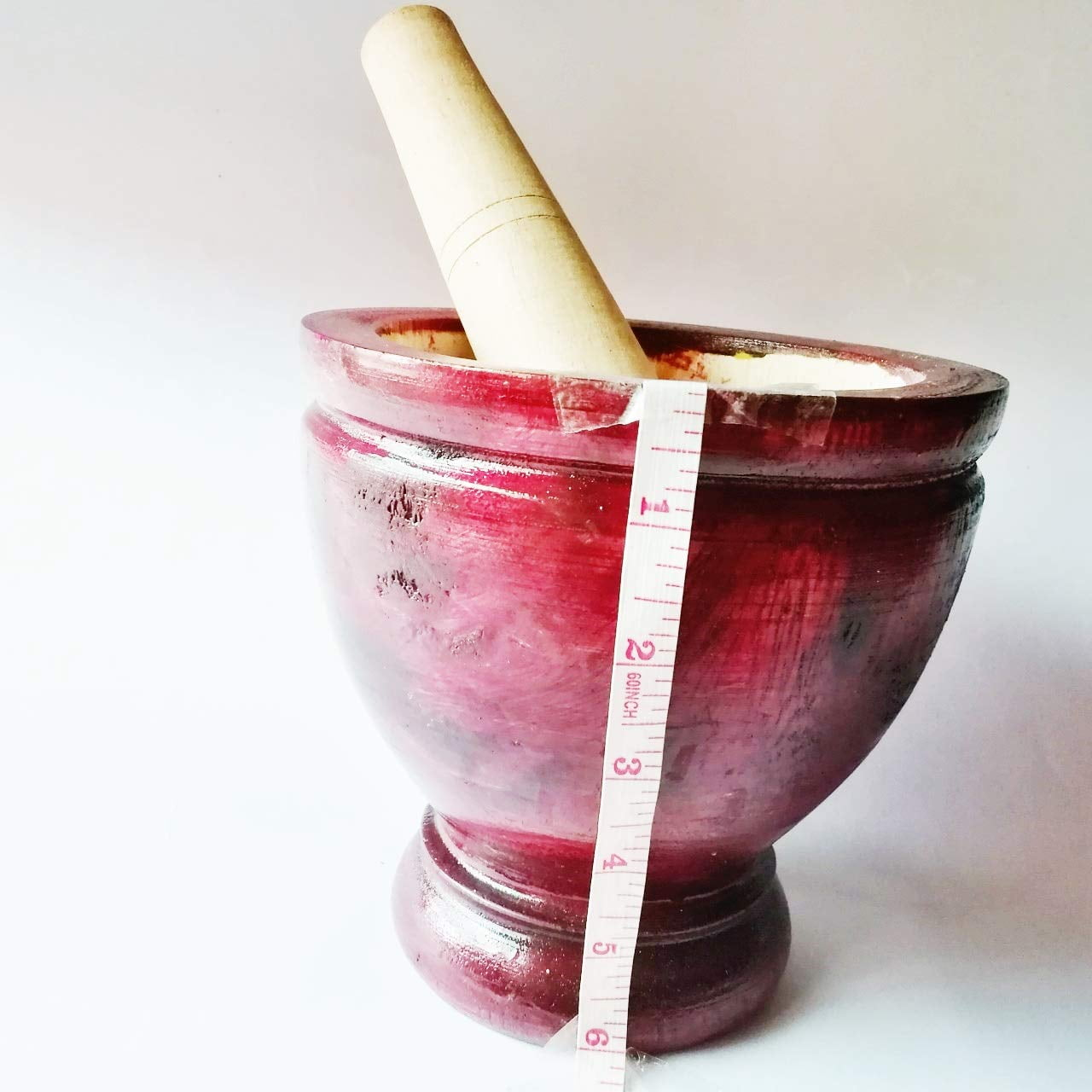 Ein roter Holzmörser und Stößel mit einem Maßband daneben, vor weißem Hintergrund.