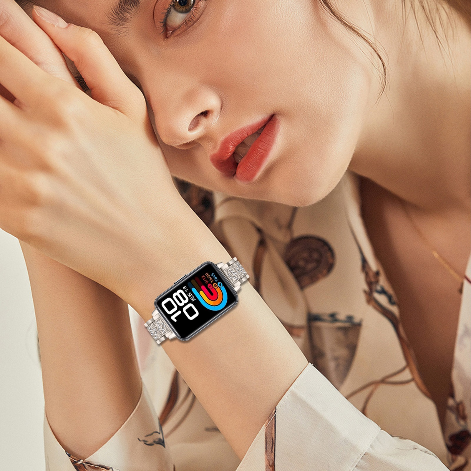 Frau mit Smartwatch und Silberband. Das Zifferblatt zeigt Zeit und Infos. Sie trägt ein Oberteil mit Blumenmuster.