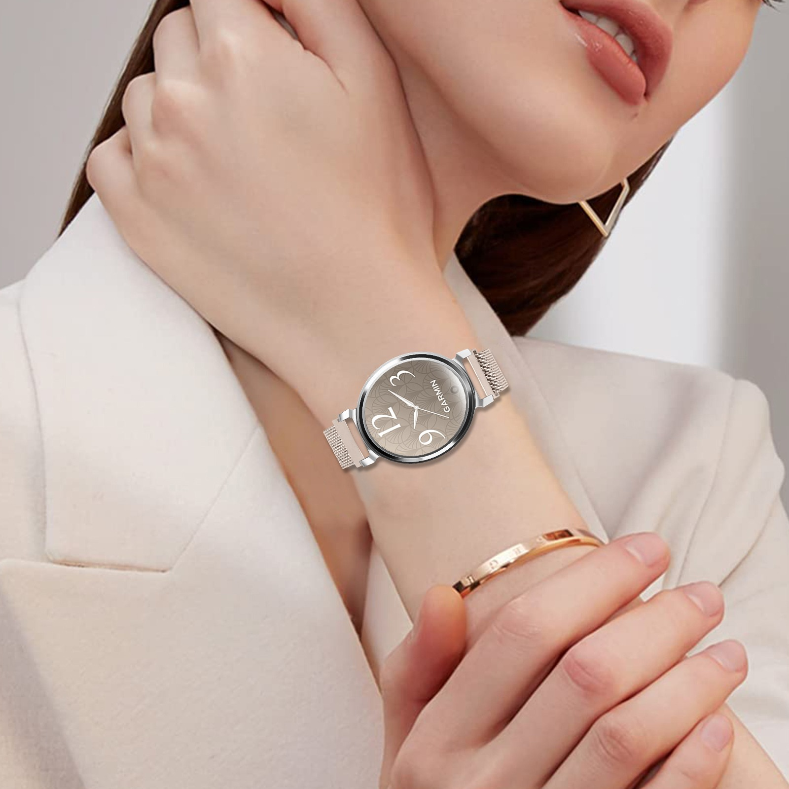 Das Handgelenk einer Frau zeigt eine Garmin-Uhr mit silbernem Armband. Ein goldenes Armband befindet sich am anderen Handgelenk.