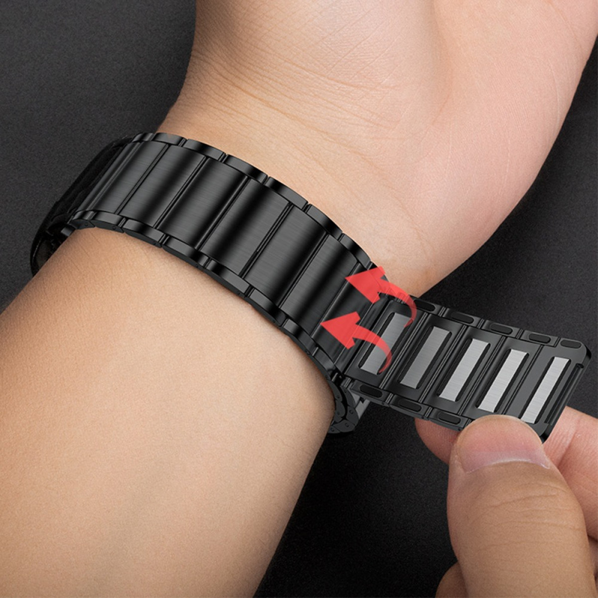 Ein schwarzes Armband wird am Handgelenk geschlossen. Rote Pfeile zeigen die Bewegung des Verschlusses. Eine Hand hält das Band.