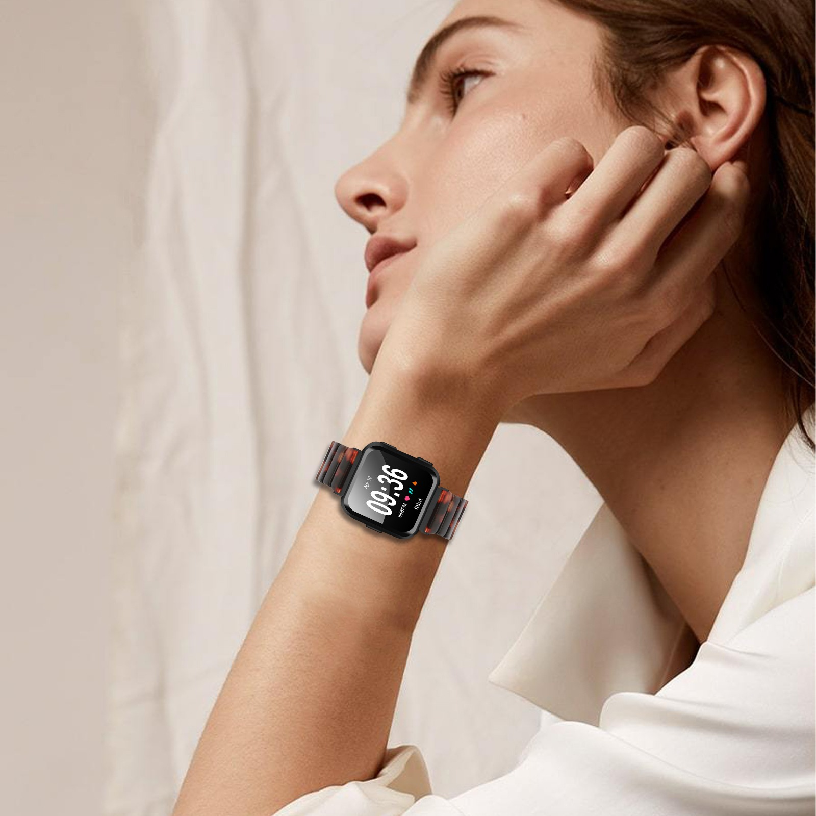 Eine Frau trägt eine Smartwatch mit der Anzeige 09:36. Sie berührt ihr Ohr. Die Uhr hat ein gemustertes Armband.