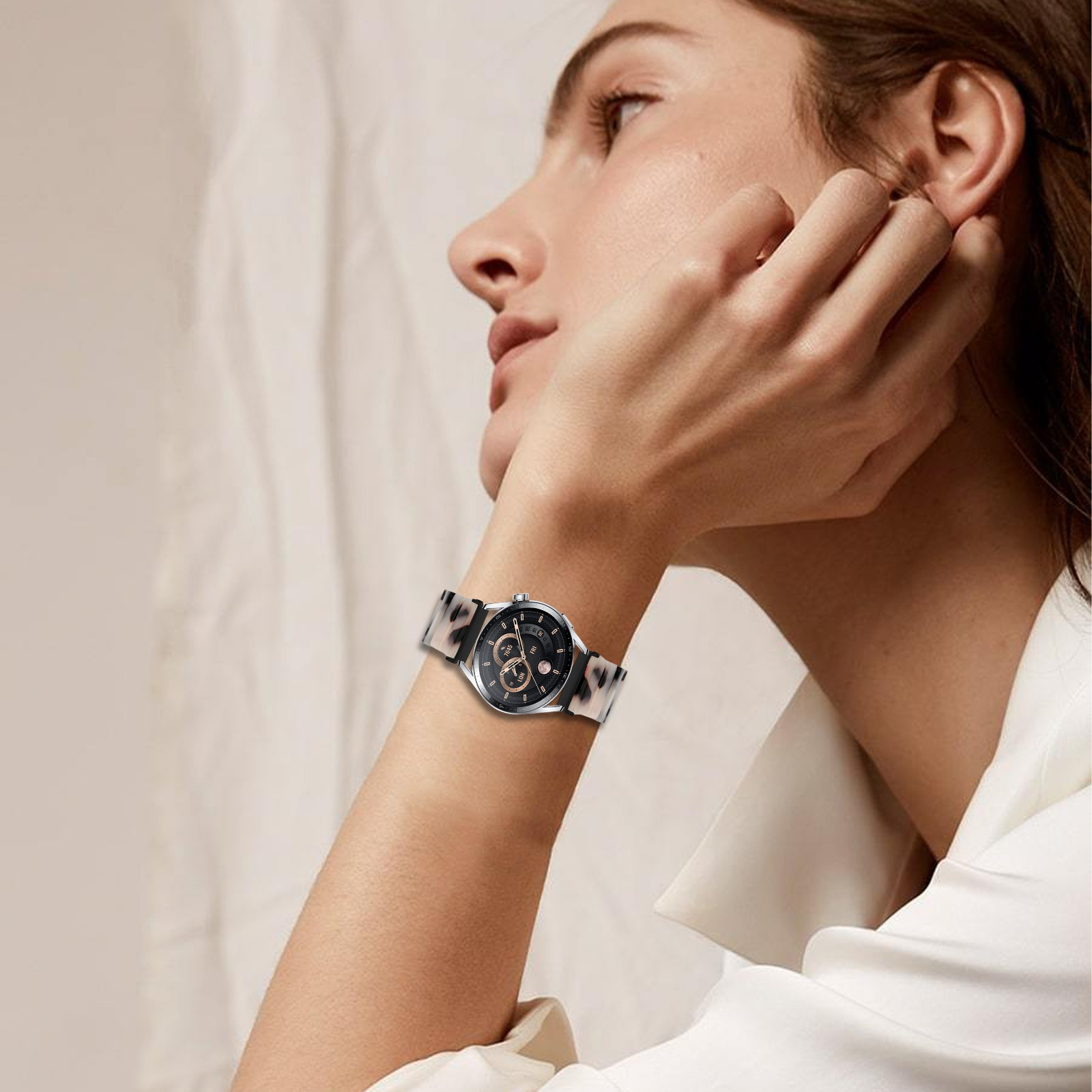 Una donna che indossa un orologio con cinturino fantasia. La sua mano è vicino al viso. Lo sfondo è bianco.