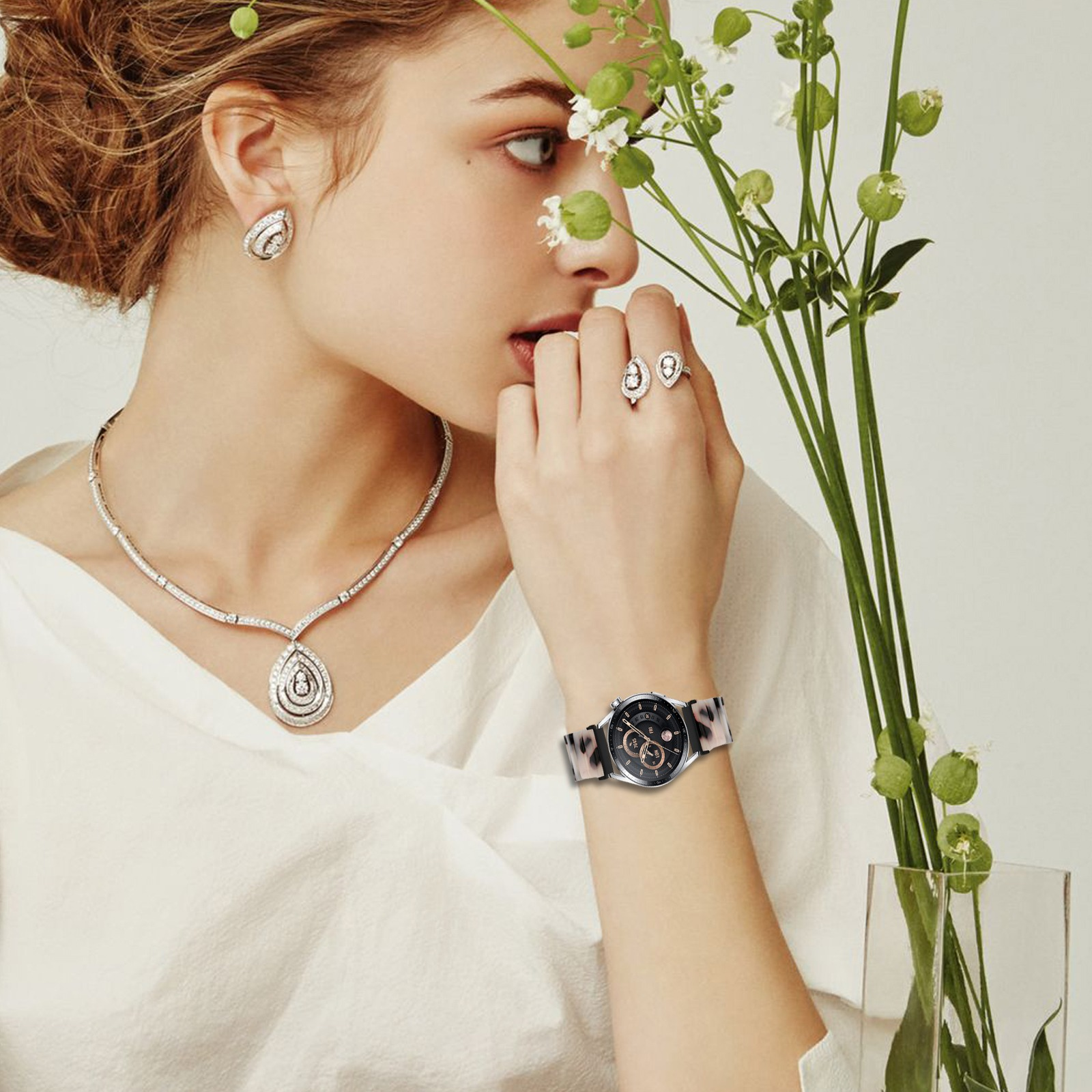 Una donna con gioielli e un orologio tiene dei fiori. Indossa un top bianco. I gioielli includono orecchini, una collana e anelli.