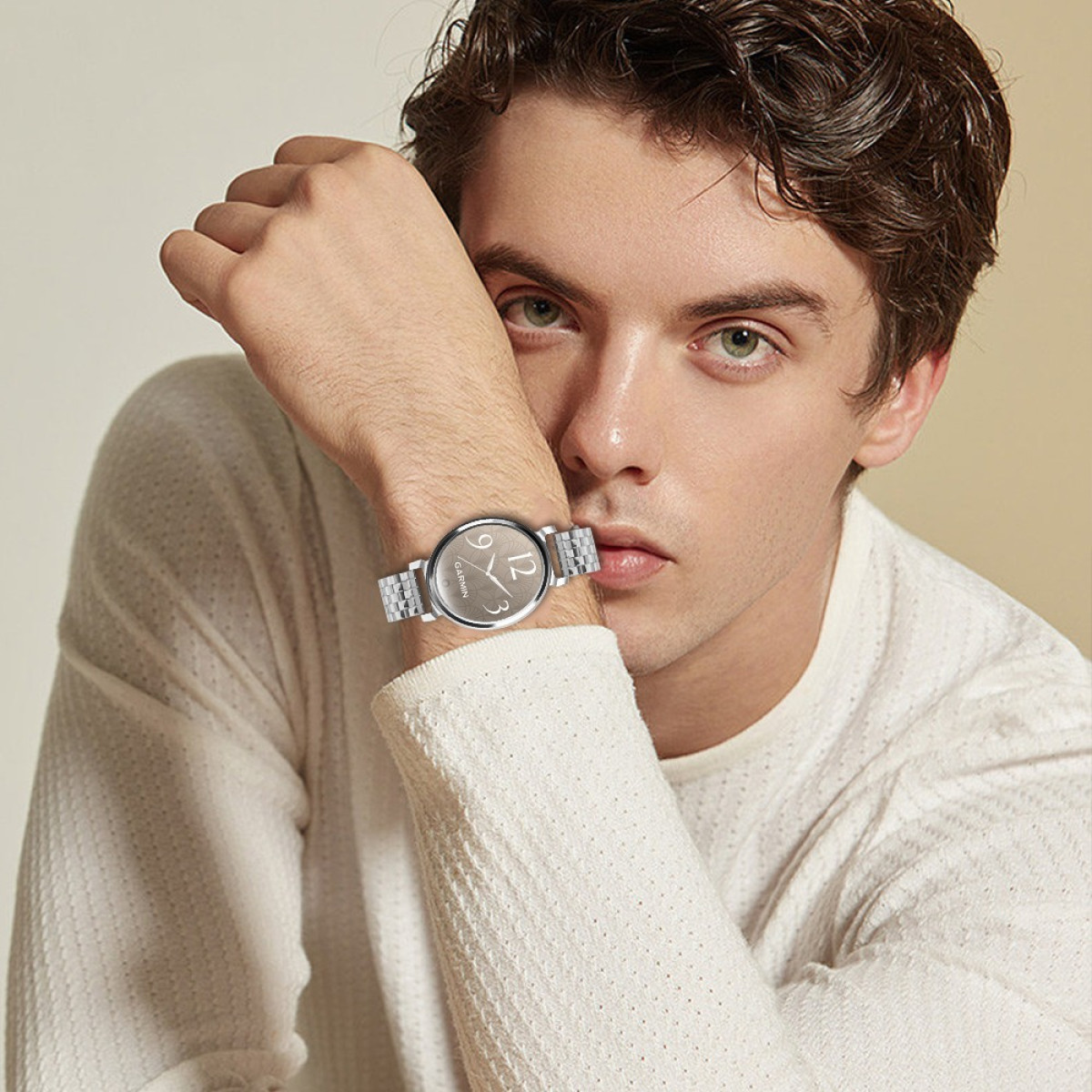 Un uomo con un orologio. L'orologio ha un cinturino argentato e un quadrante marrone chiaro con il numero 12 visibile. Indossa una camicia bianca.