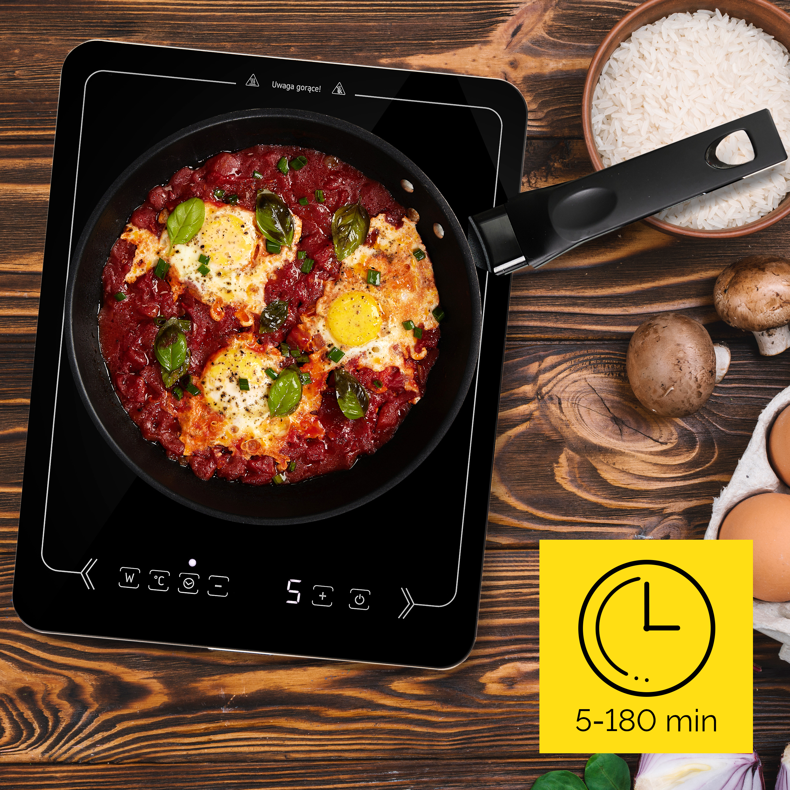 Patelnia z jajkami i sosem pomidorowym na czarnej płycie indukcyjnej, z ryżem, jajkami i grzybami.