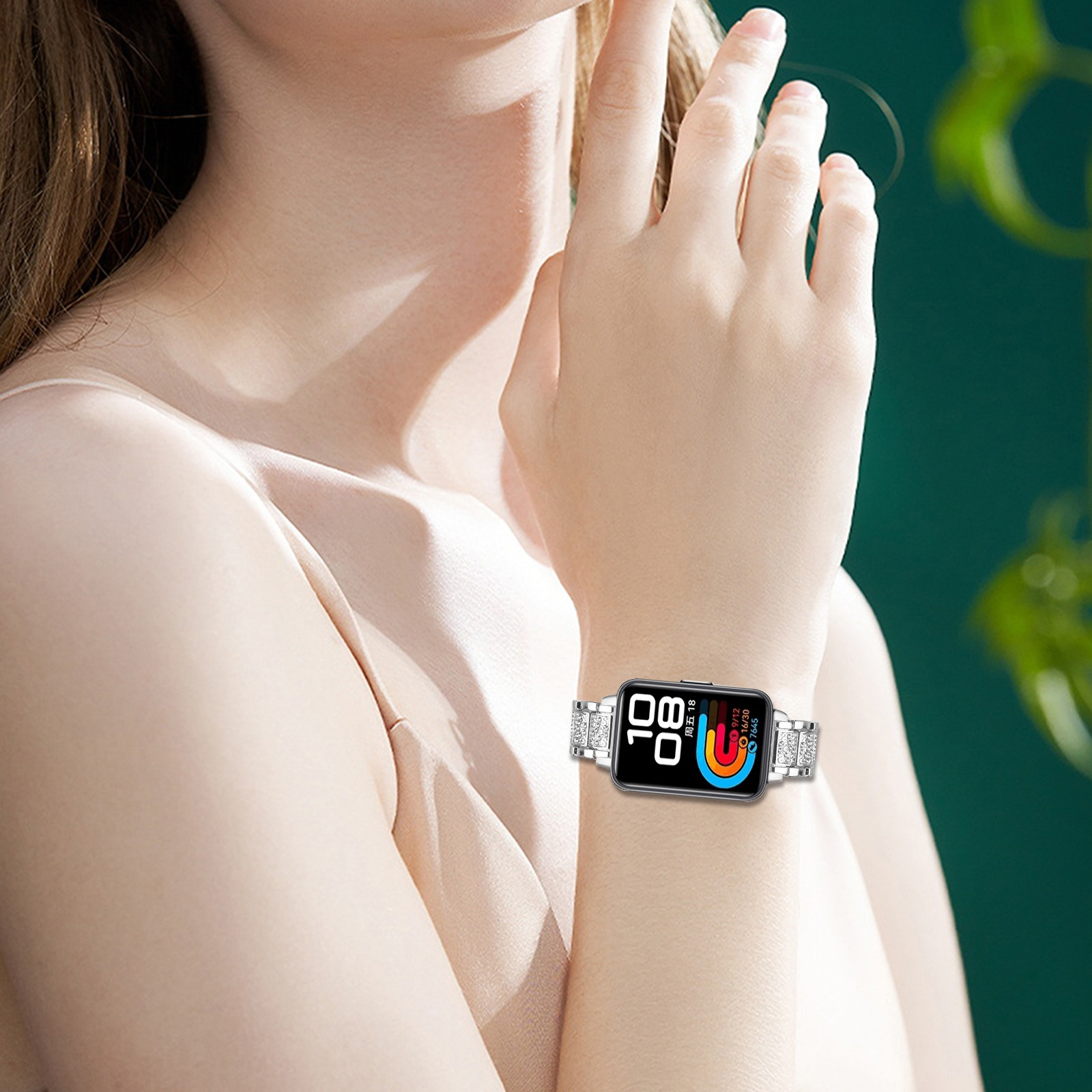 Arm einer Frau mit Smartwatch. Die Uhr zeigt Zeit und farbigen Gesundheitsgraphen. Der Hintergrund ist grün verschwommen.