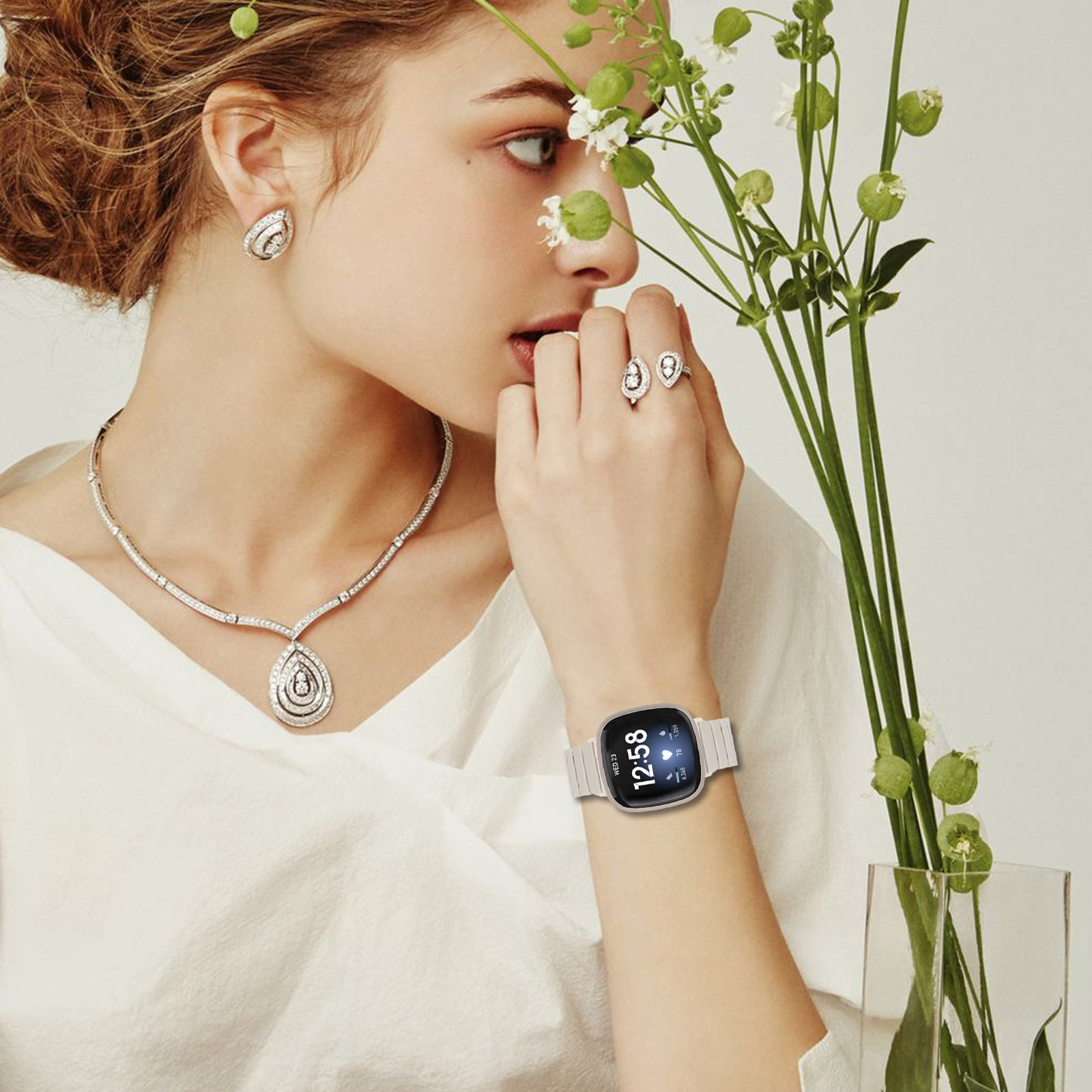 Frau mit Schmuck und Smartwatch, hält Blumen. Sie hat eine Halskette, Ohrringe und einen Ring.