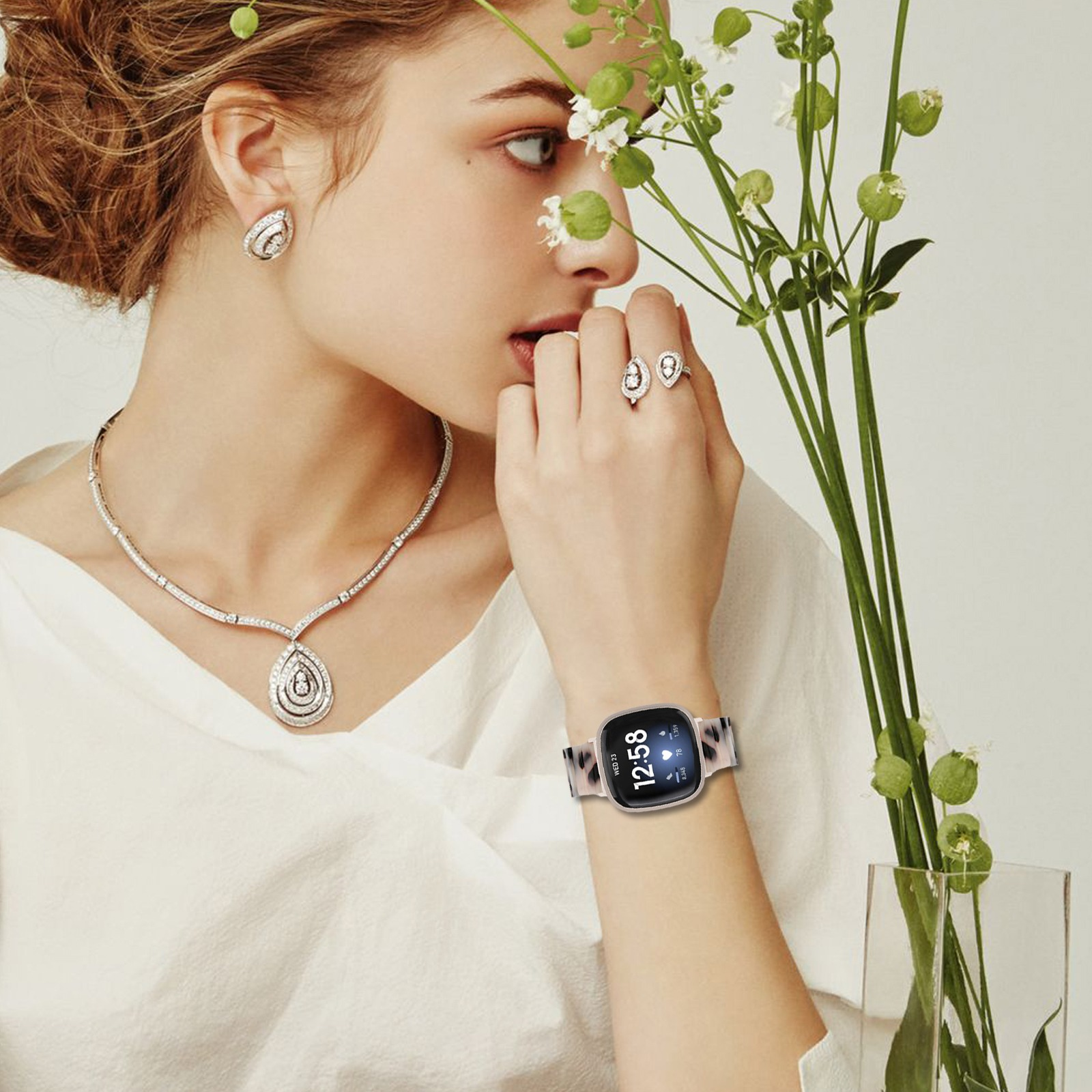 Frau mit Schmuck und Smartwatch, hält Blumen. Accessoires sind Ohrringe, Halskette und Ringe. Gezeigte Zeit: 12:58.