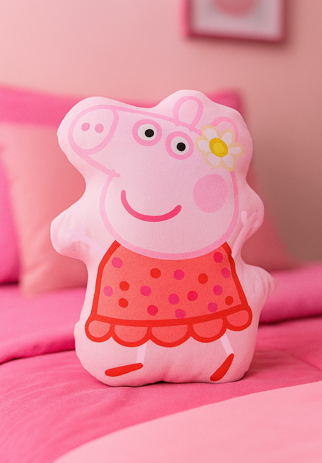 Rosa Peppa Wutz Kissen auf einem rosa Bett. Es hat ein rotes Kleid mit rosa Punkten und eine Gänseblümchen auf dem Kopf.