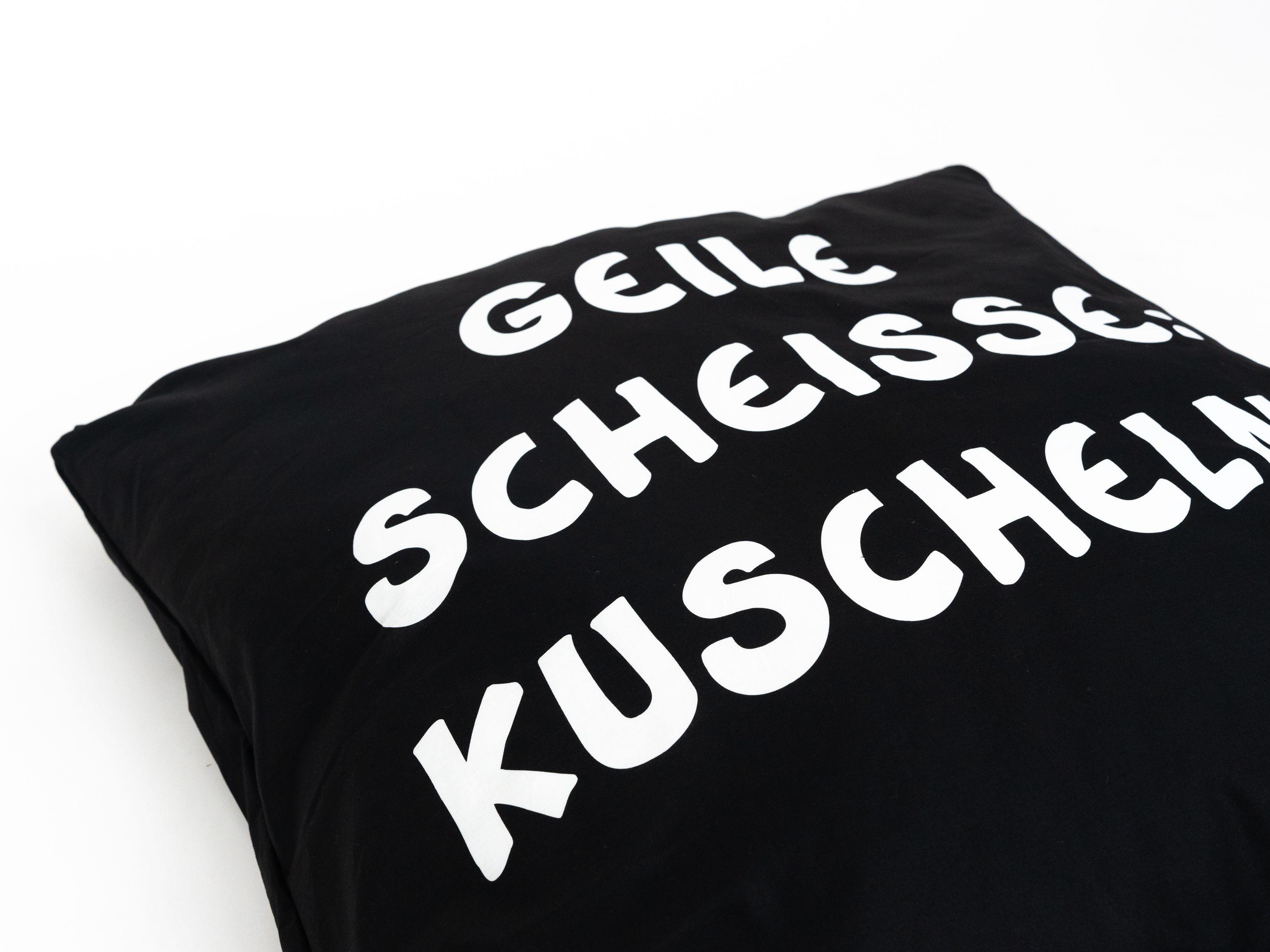Schwarzes Kissen mit weißem Text, der 'GEILE SCHEISSE KUSCHEL' sagt.