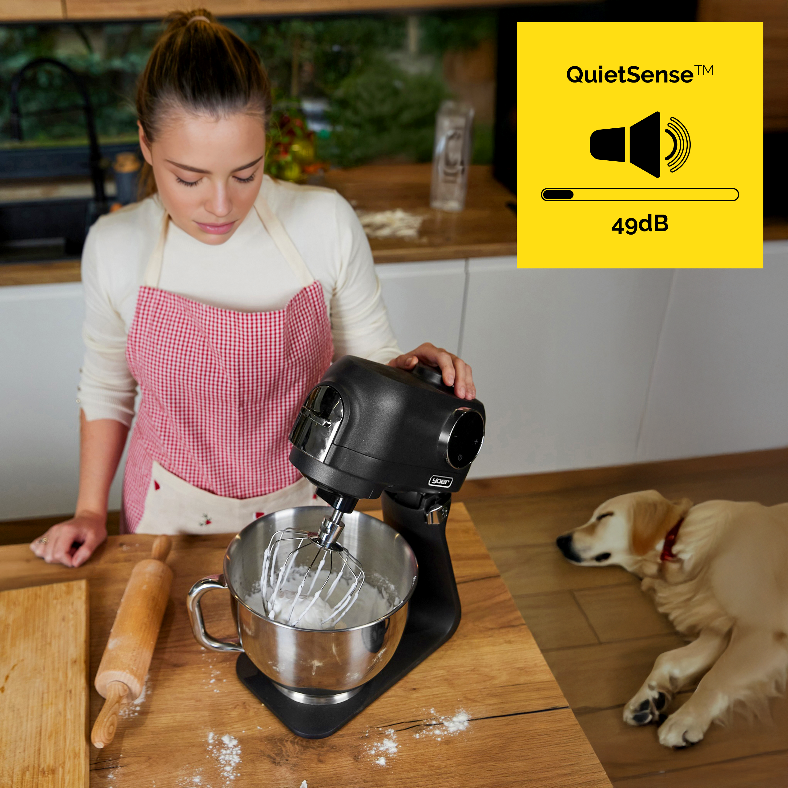 Kobieta w kuchni używa miksera. Pies leży na podłodze. Żółty znak pokazuje dźwięk przy 49dB.