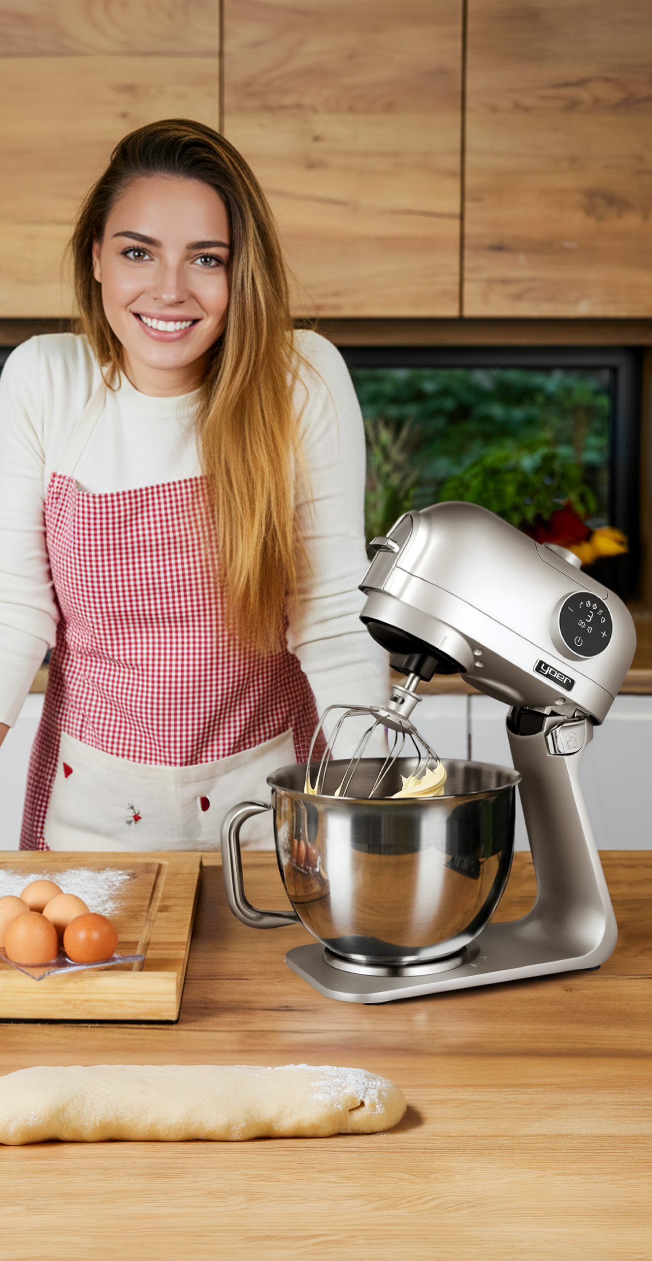 Kobieta w kuchni z mikserem, fartuchem, jajkami i ciastem. Uśmiecha się do kamery. Tło: drewniane szafki i okno.