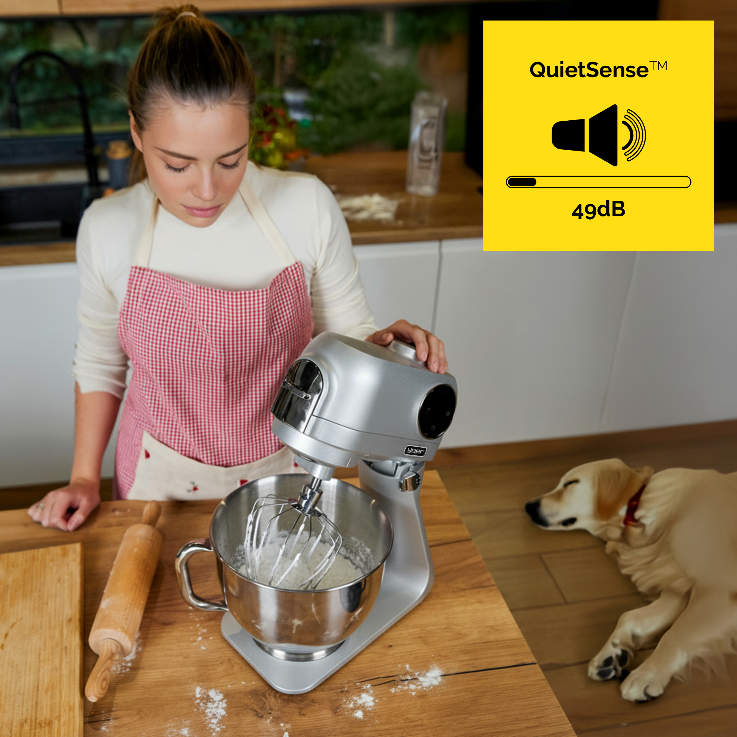 Kobieta w kuchni używa miksera, pies leży na podłodze. Etykieta QuietSense pokazuje 49dB.