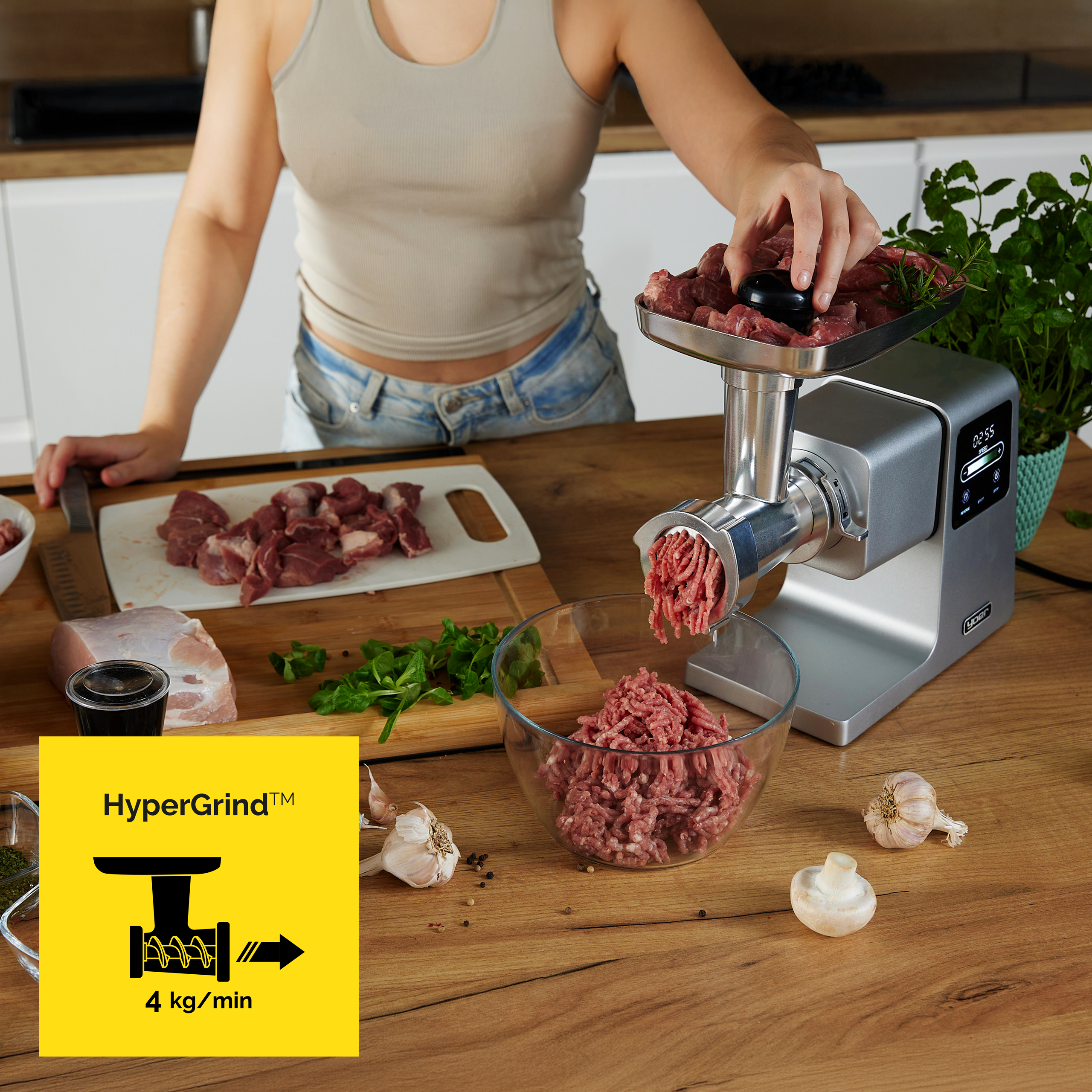 Kobieta mieli mięso w maszynce. Na blacie czosnek, grzyby i zioła.