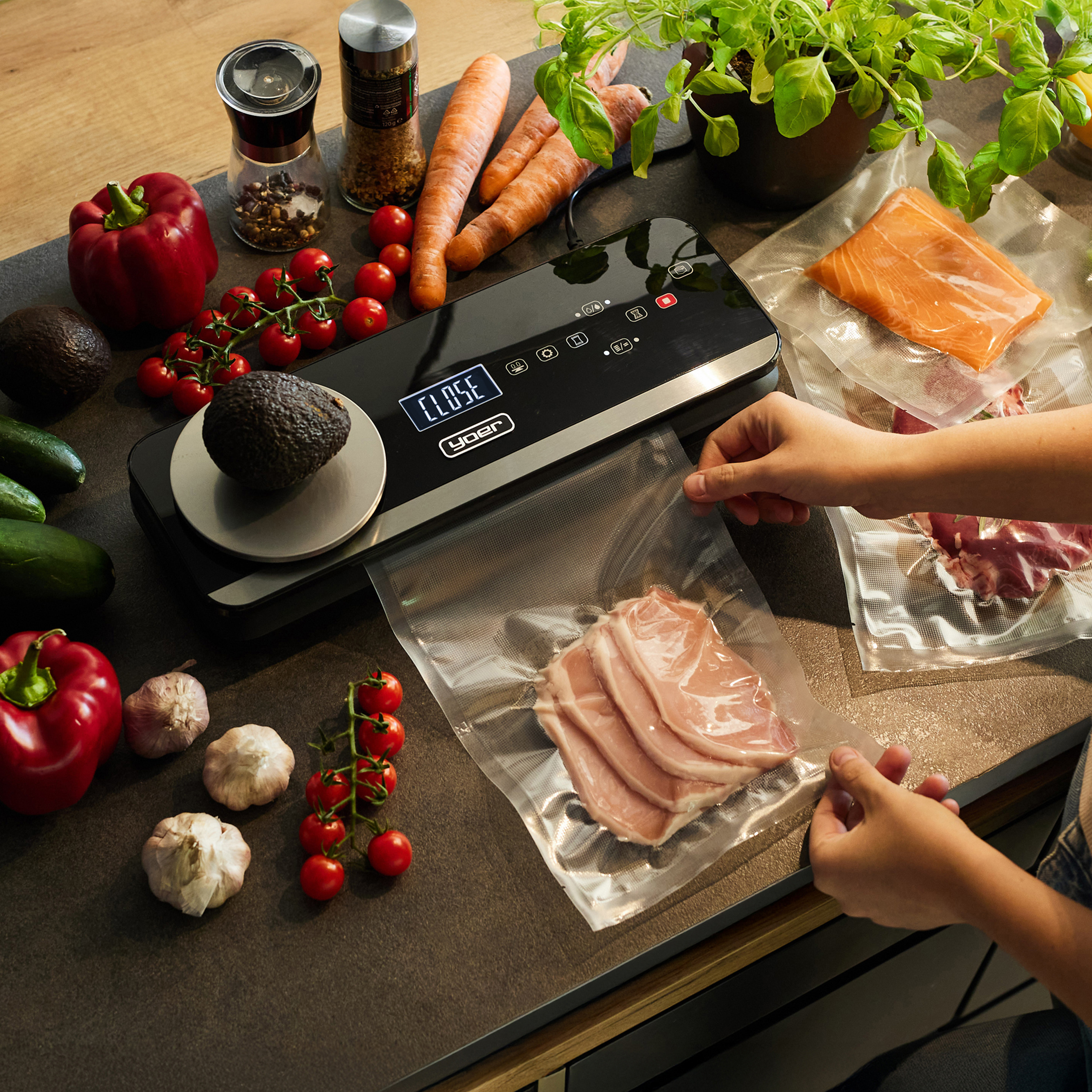 Scena kuchenna ze składnikami i zgrzewarką próżniową. Zawiera warzywa, mięso i zioła. Ręce zamykają worek z kotletami schabowymi.