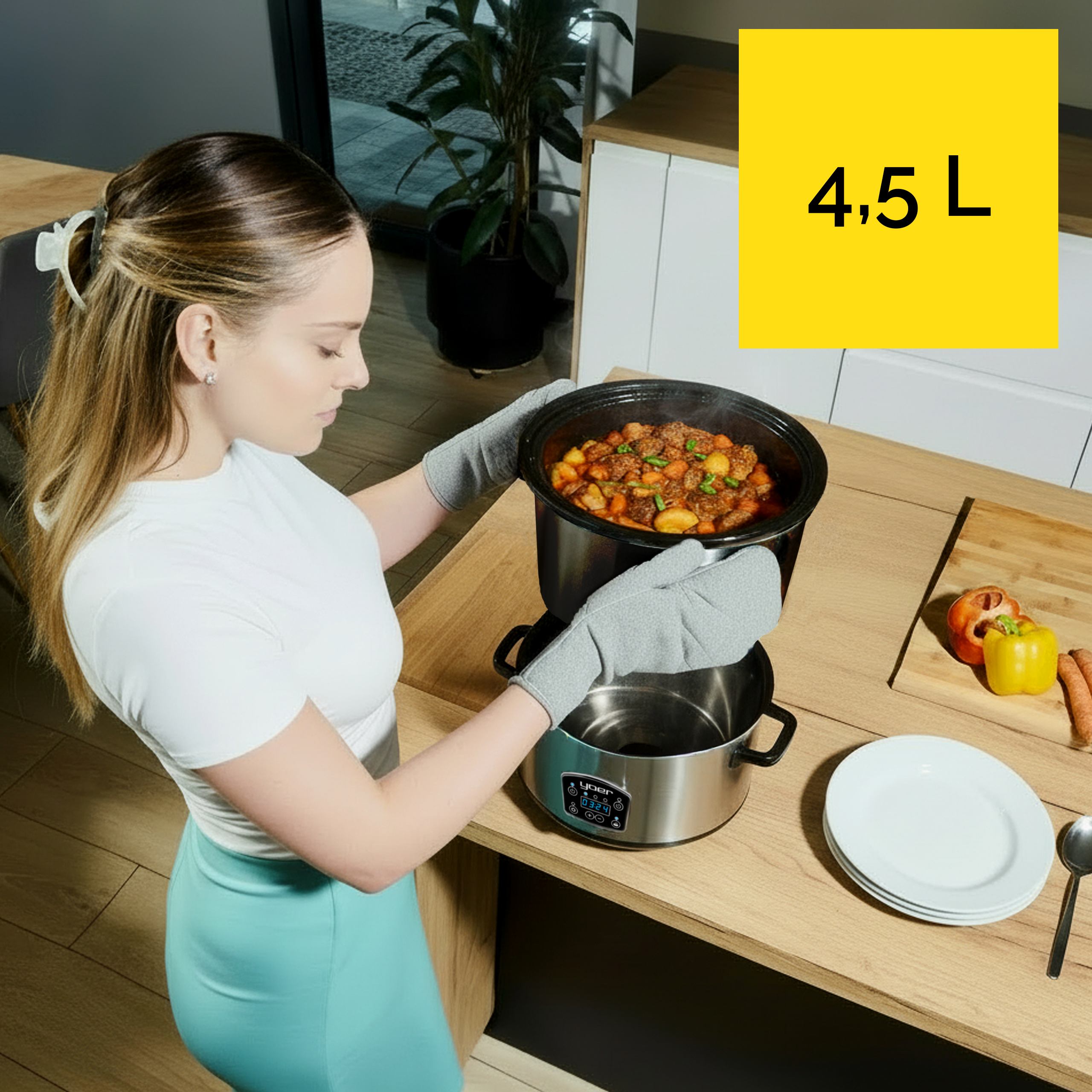 Kobieta trzyma wolnowar z jedzeniem. Żółty znak mówi 4,5 L. Talerze i warzywa na stole.