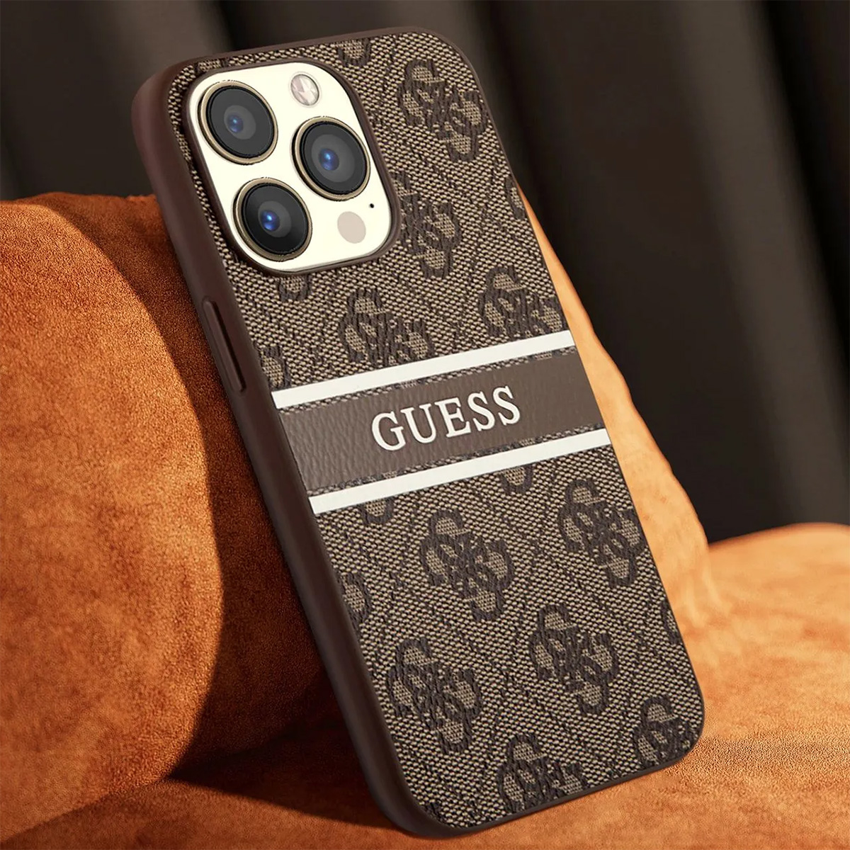Una custodia per telefono Guess marrone con motivo monogramma e logo Guess. La custodia è su una superficie marrone-arancione.
