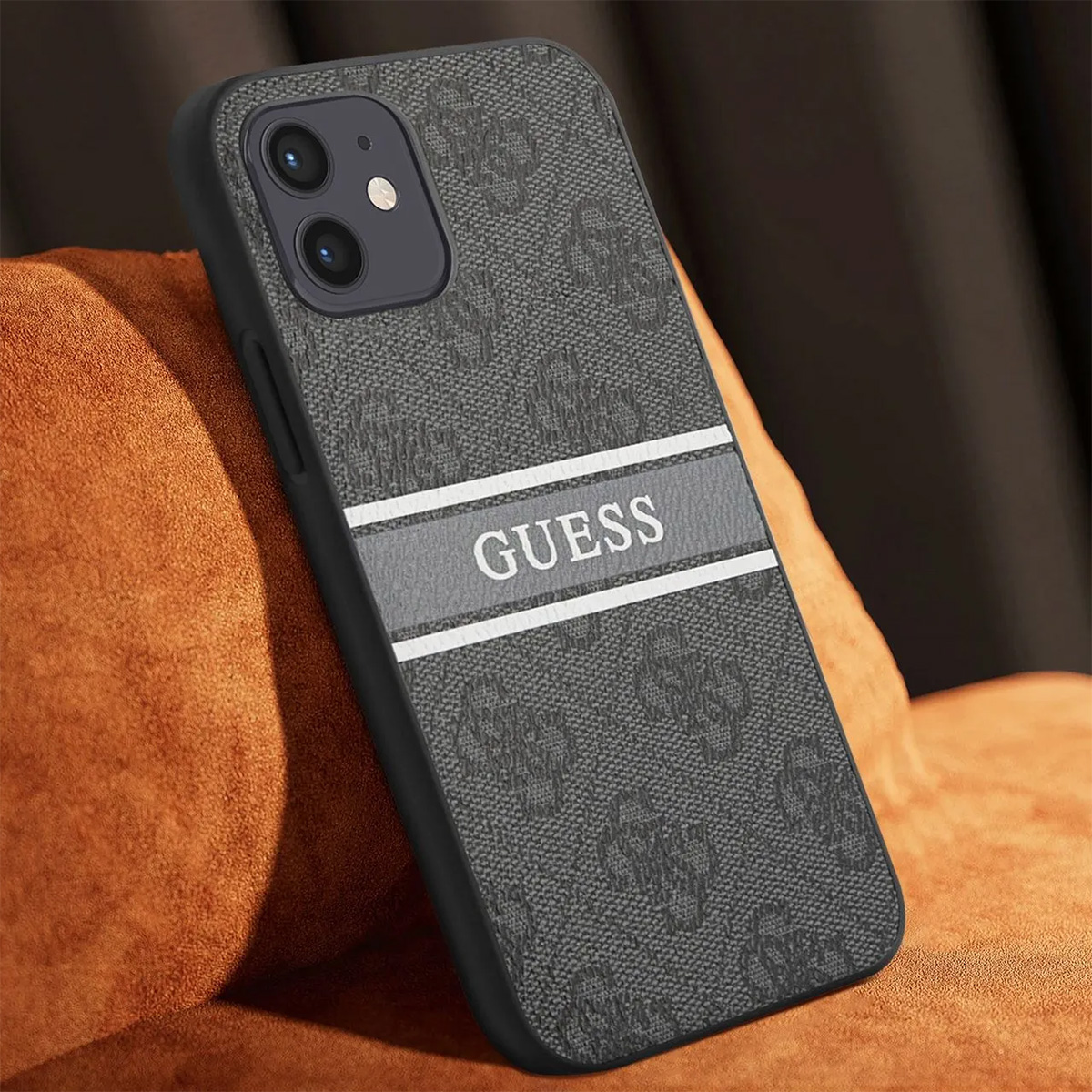 Una custodia per telefono Guess con un motivo grigio e una sezione a strisce bianche con il nome del marchio. Poggia su una superficie arancione.