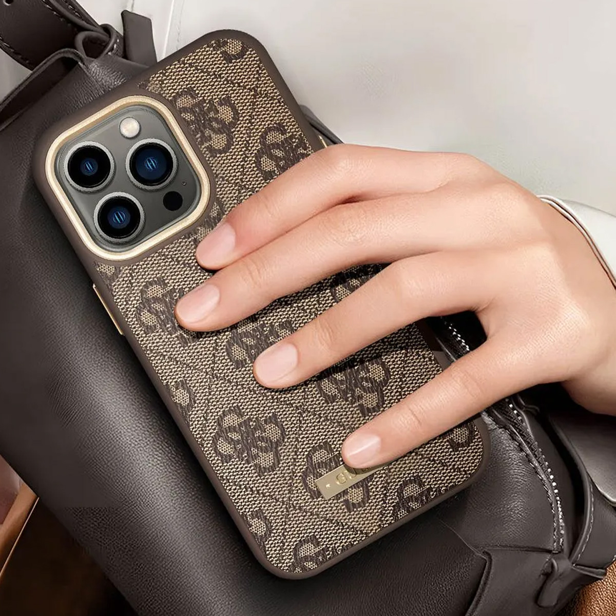 Una mano tiene in mano un telefono in una custodia fantasia. Il telefono è appoggiato su una borsa di pelle marrone scuro. Lo sfondo è sfocato.