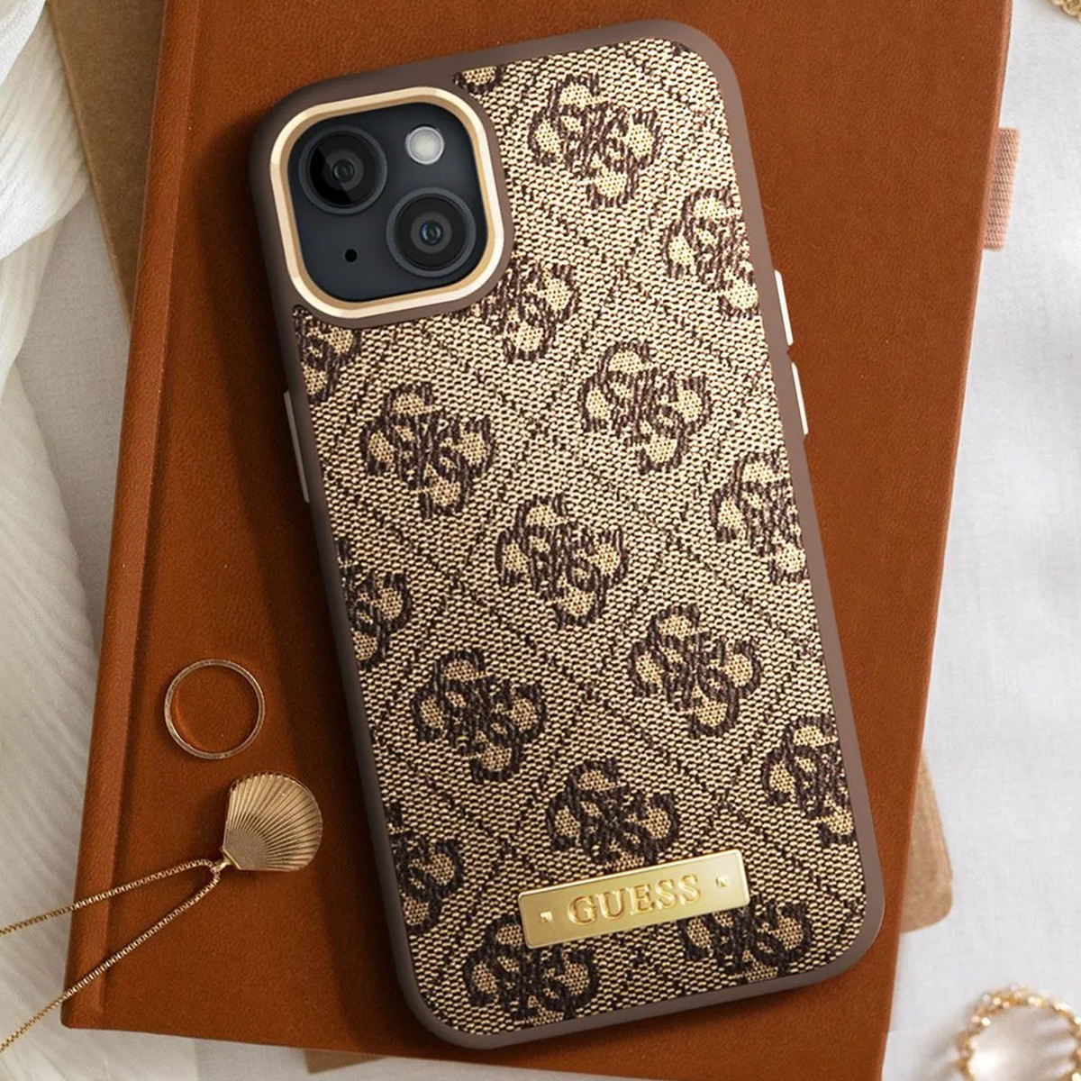 Un iPhone in una custodia Guess, marrone con motivo logo, su un taccuino marrone. Un anello e una collana sono anche sul taccuino.