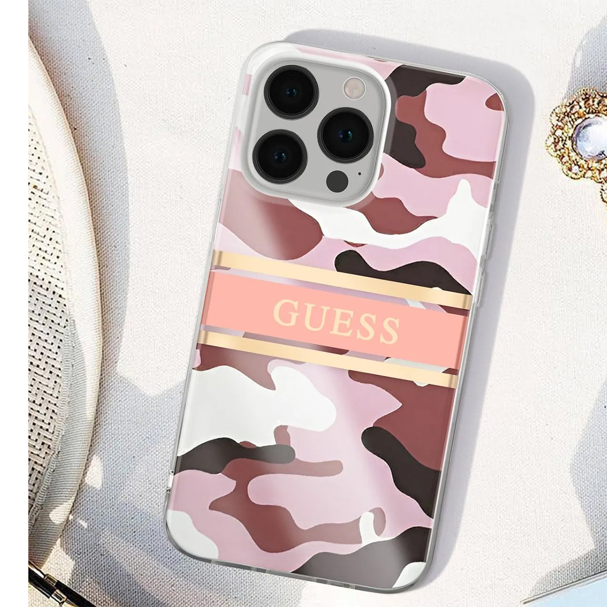 Una custodia per telefono con motivo mimetico rosa e la scritta 'GUESS'. La custodia ha un bordo trasparente e diverse lenti.