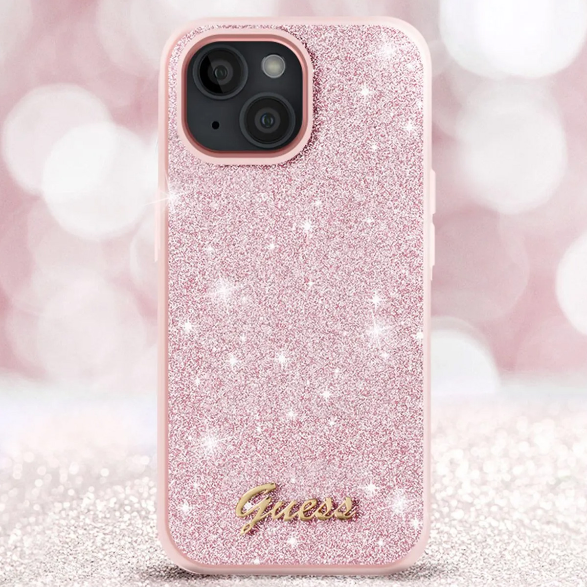 Una custodia per iPhone rosa glitterata con il logo Guess. La custodia ha un ritaglio per la fotocamera e si trova su uno sfondo bokeh.