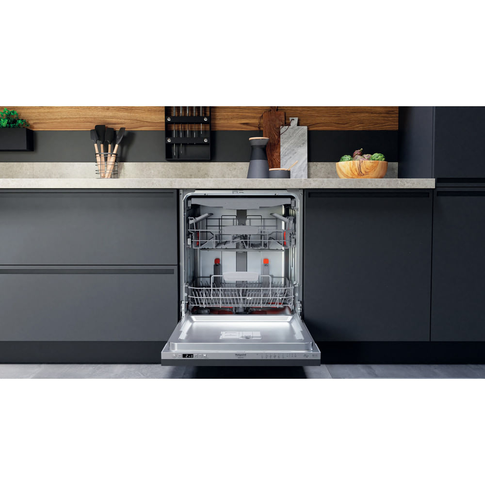 Una lavastoviglie aperta in una cucina moderna. Armadi scuri, dettagli in legno e una ciotola di cibo sono visibili.
