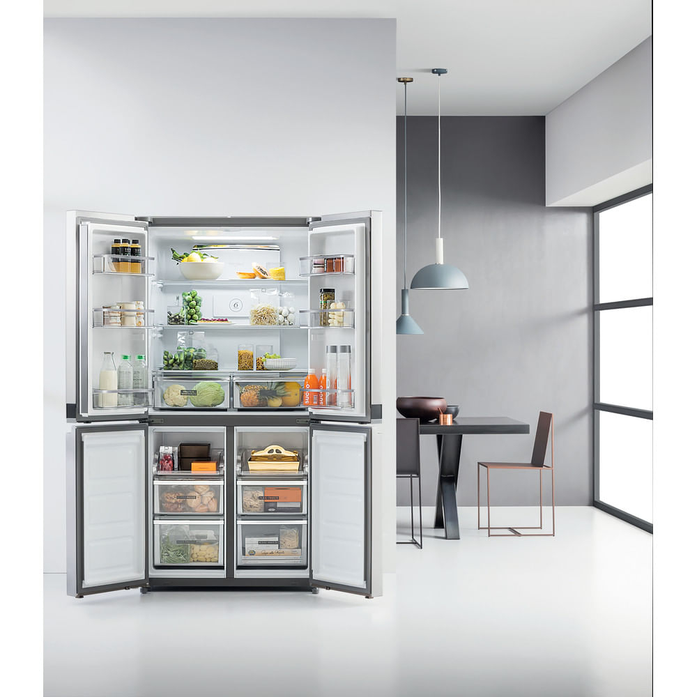 Refrigerador abierto lleno de comida. Interior de cocina con mesa, sillas y lámparas colgantes. Diseño brillante y moderno. Tonos blancos y grises.