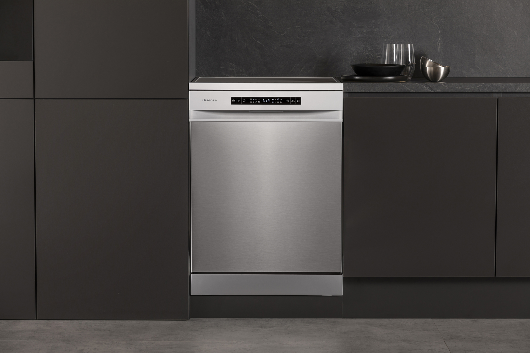 Lavastoviglie in acciaio inox in cucina scura, con mobili e piano neri. Bicchiere e ciotole.