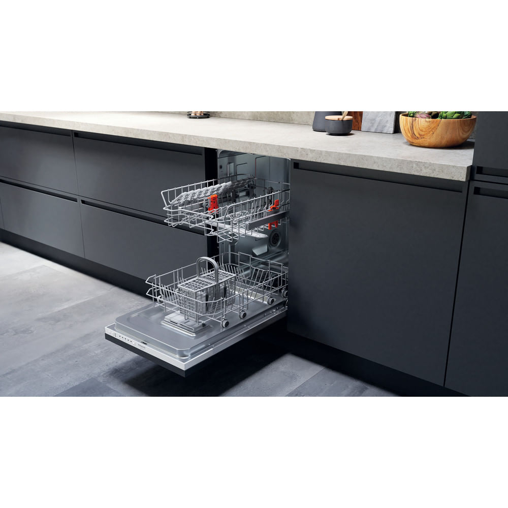 Lavastoviglie aperta con due cestelli. Armadietti e piano di lavoro grigi. Ciotola di legno e altri oggetti da cucina sullo sfondo.