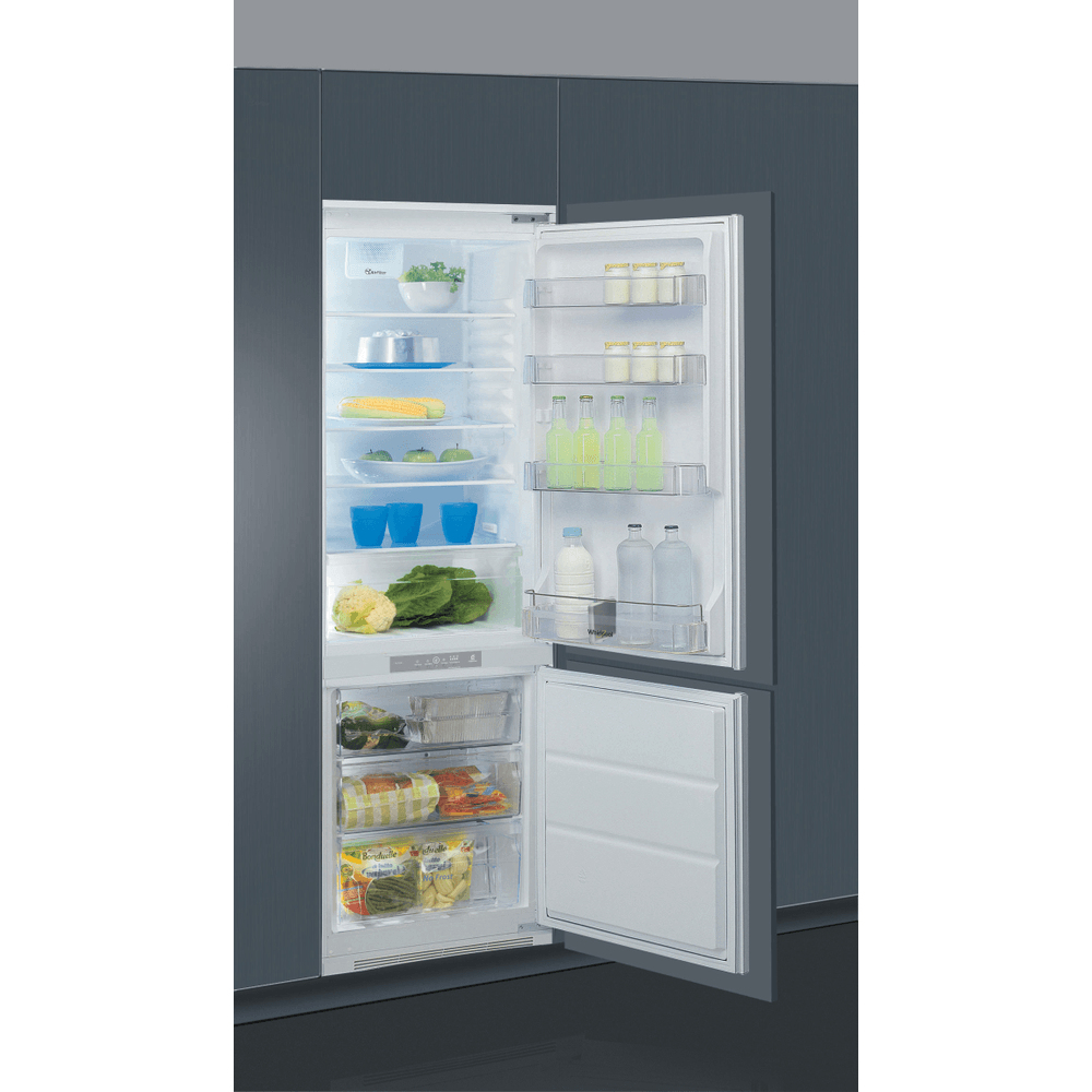 Frigorifero bianco aperto con cibo all'interno. Include verdure, bevande e latticini sugli scaffali. Il cassetto del congelatore è aperto.