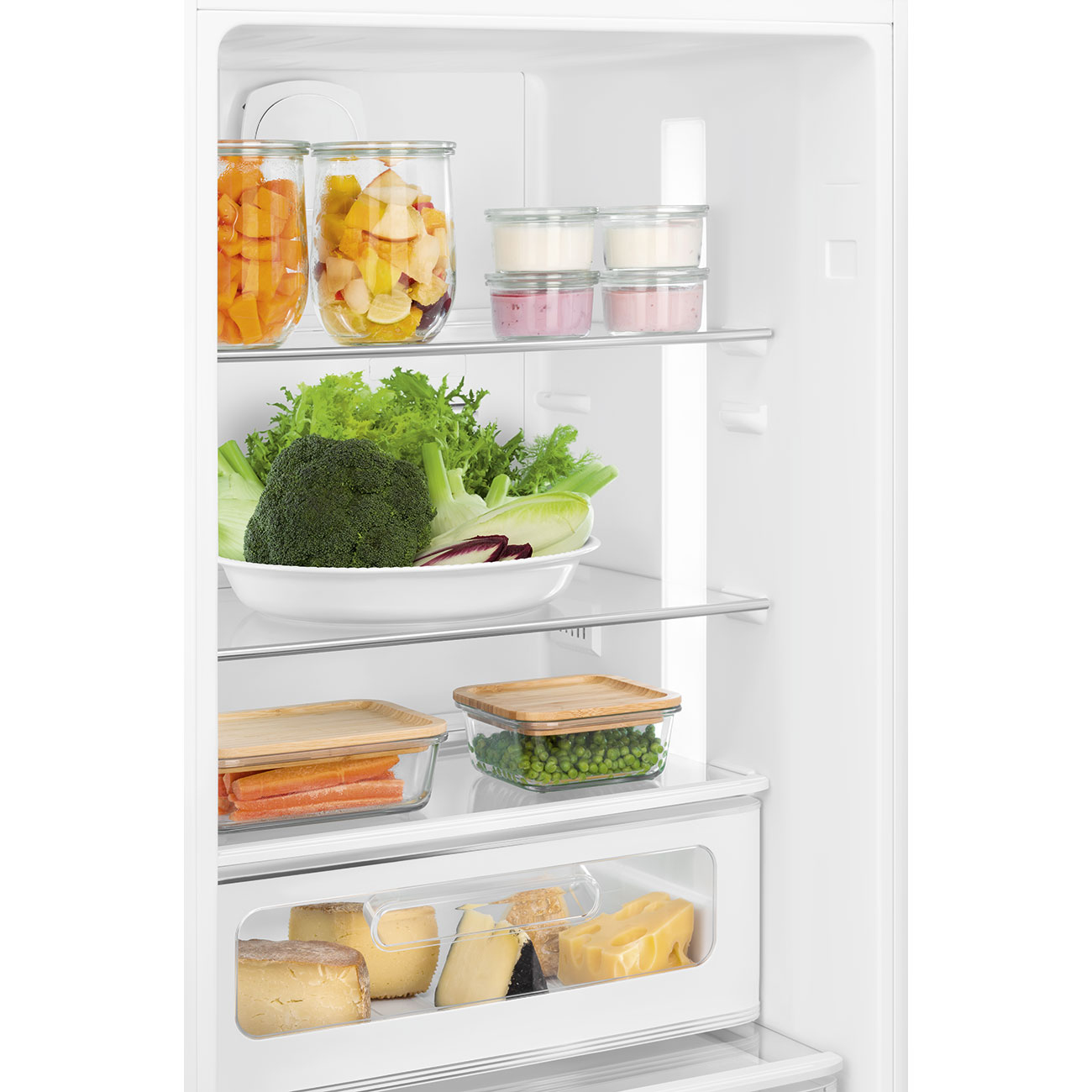 Interior de la nevera lleno de alimentos: frutas, verduras y quesos. Se ven frascos, recipientes y un plato blanco.
