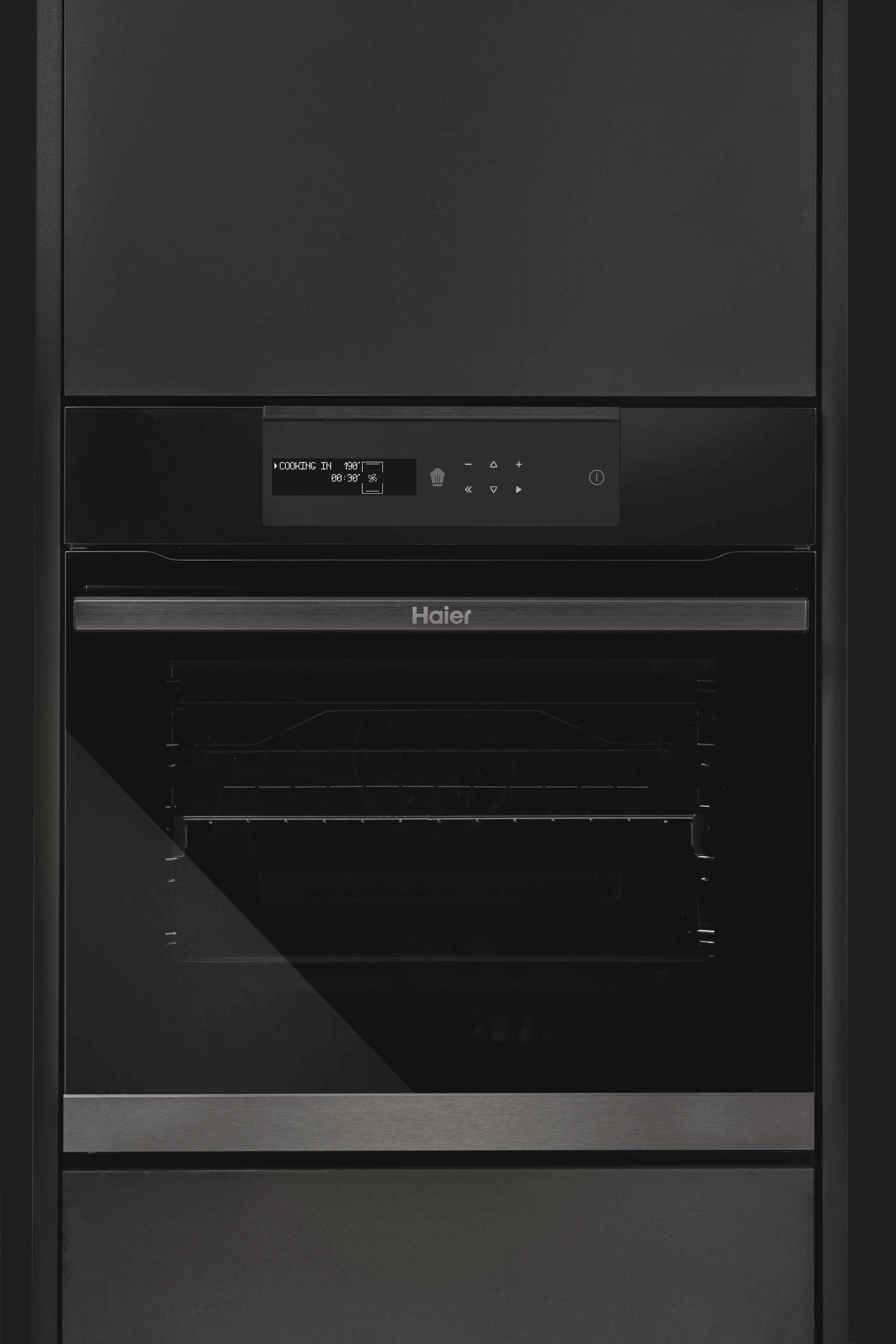 Se muestra un horno Haier negro. Tiene una pantalla digital y una puerta de vidrio. El horno está integrado en un armario oscuro.