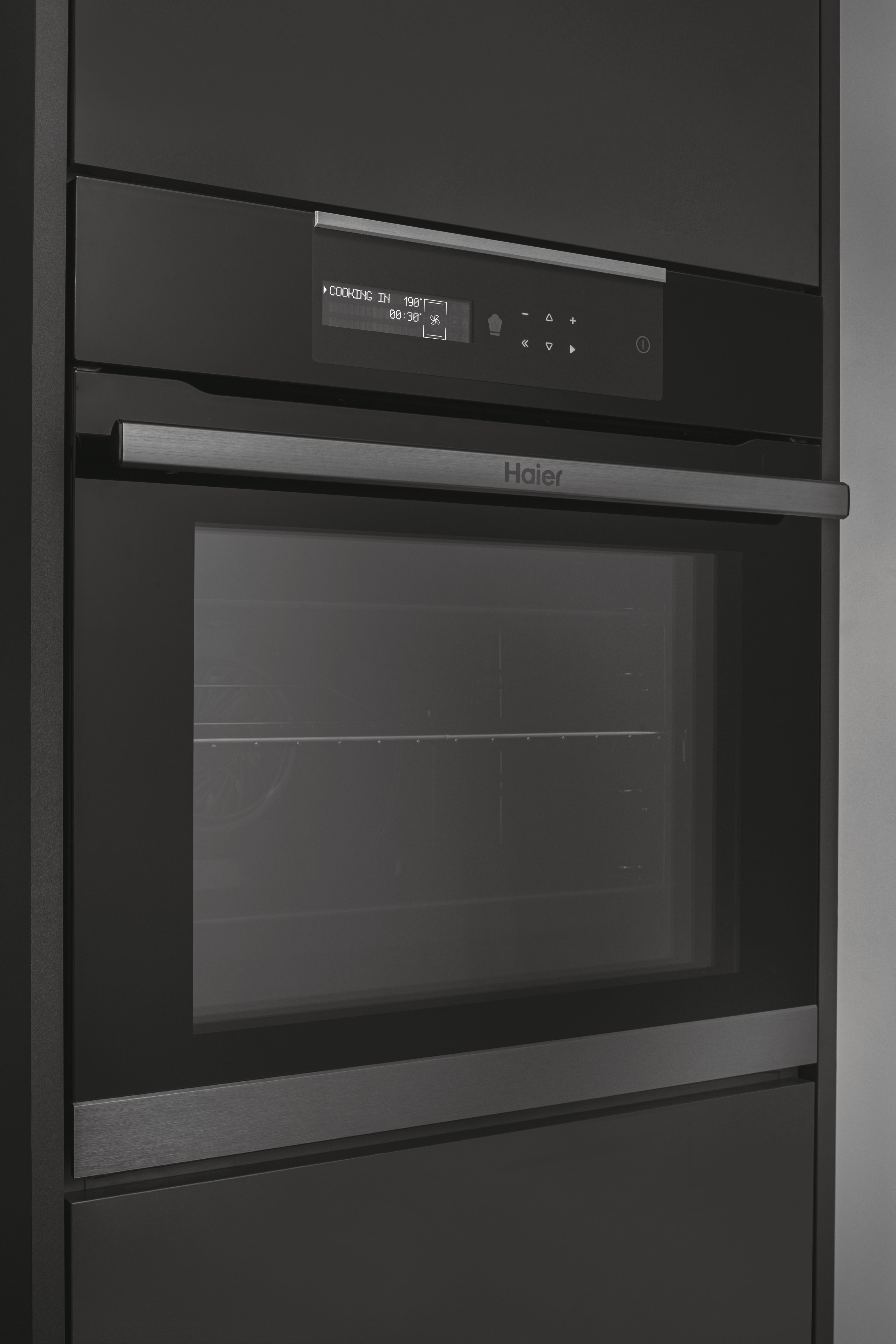 Un horno negro Haier integrado en un armario. Tiene una pantalla que muestra el tiempo y la temperatura de cocción.