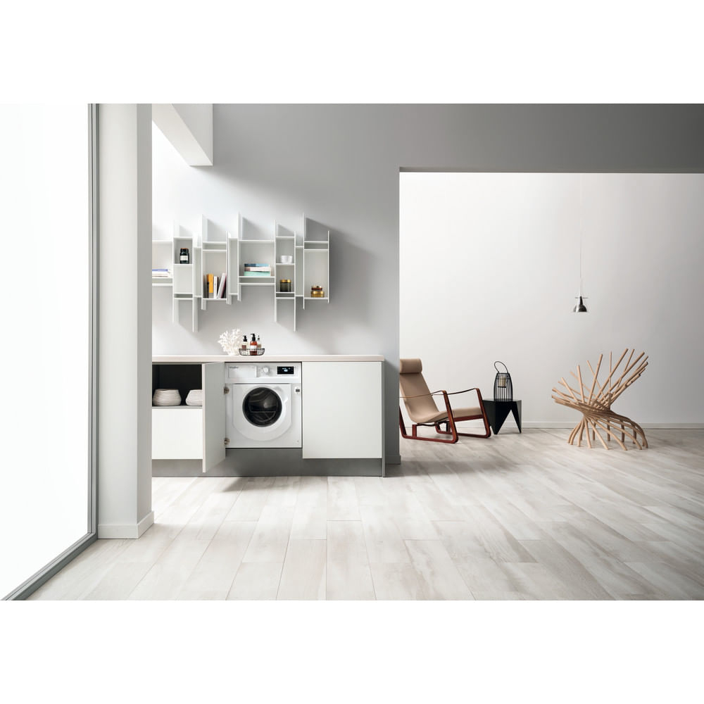 Un lavadero moderno con lavadora, armarios blancos, pisos de madera y una silla decorativa.