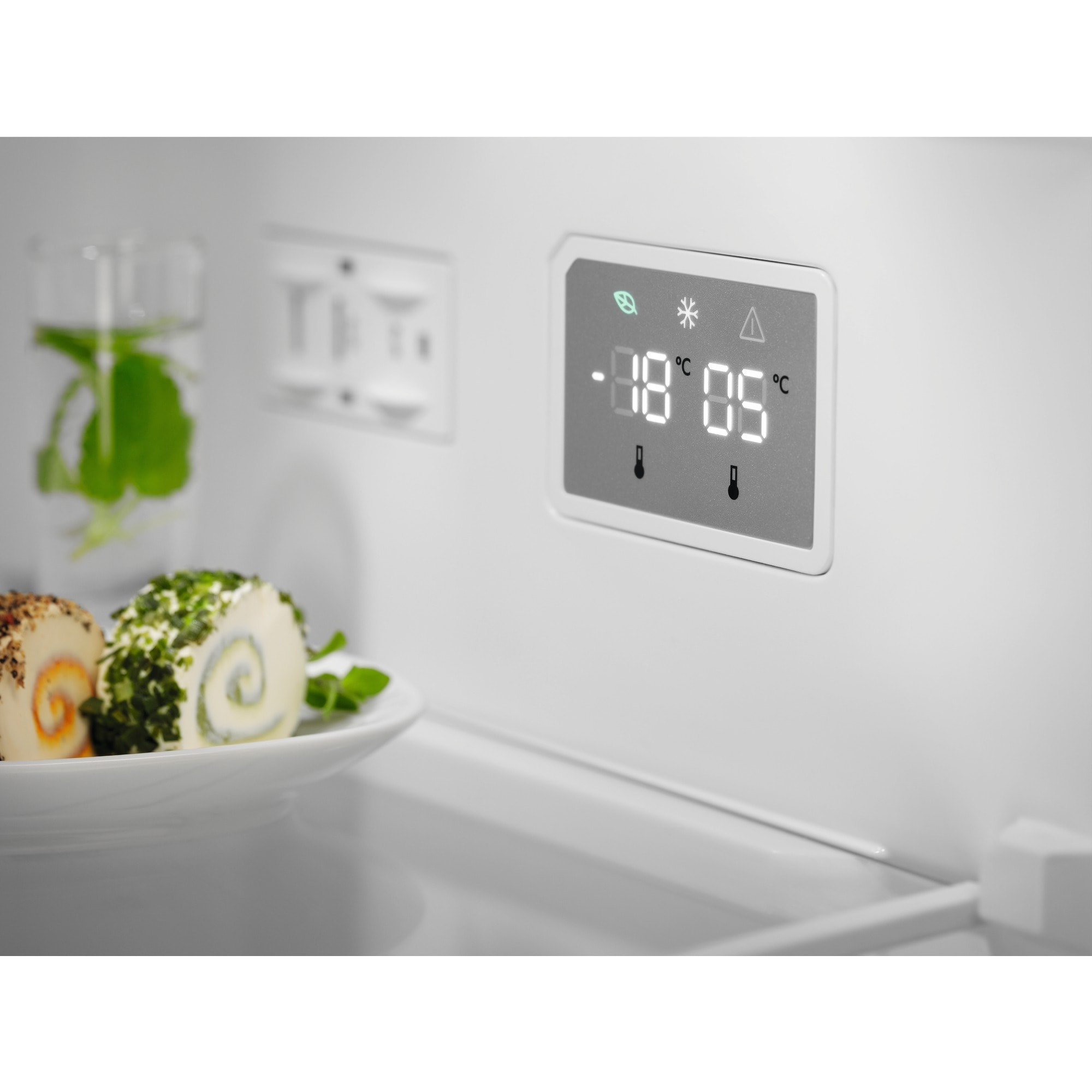 Dentro de un refrigerador, una pantalla digital muestra -18°C y 05°C. Rollos de queso en un plato y un vaso con menta.