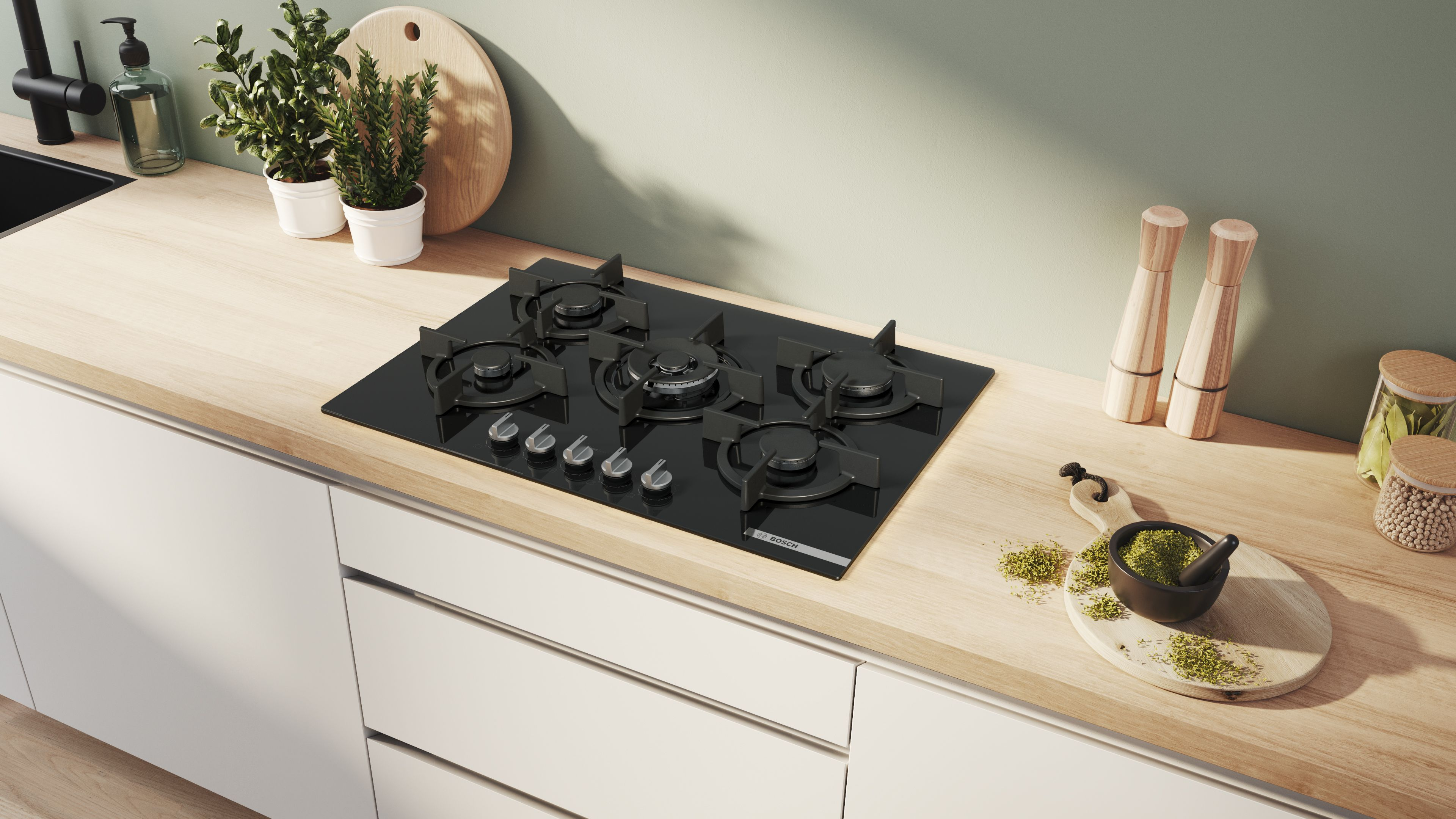 Cocina moderna con vitrocerámica negra, mortero y mazo, plantas y detalles de madera. La luz entra desde arriba a la derecha.