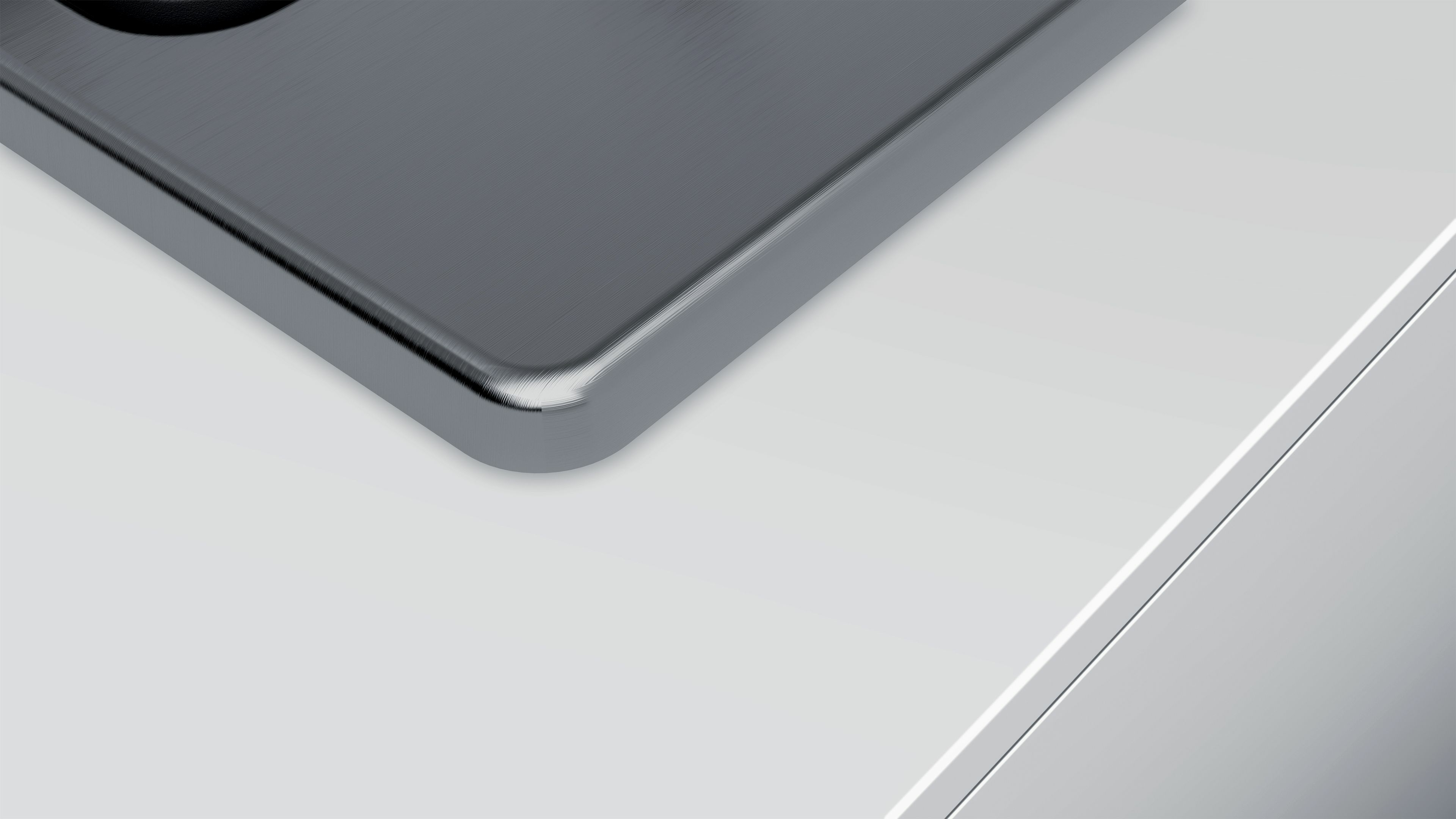 Zbliżenie metalicznego szarego rogu. Róg ma zaokrągloną krawędź. Tło jest białe i szare.