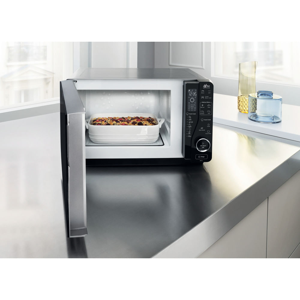 A microwave with an open door. Inside is a white dish with food. A black control panel is on the right.
