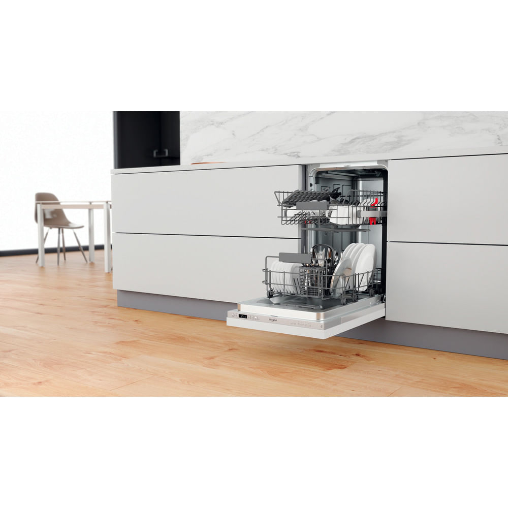 Lavastoviglie aperta con piatti all'interno. Cucina con pavimento in legno, mobili bianchi, piano in marmo e tavolo sullo sfondo.