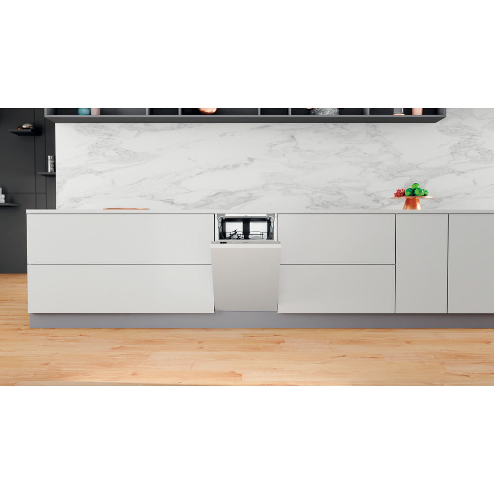 Cucina con mobili bianchi, lavastoviglie e alzatina in marmo. Pavimento in legno. Articoli decorativi verdi e rossi.