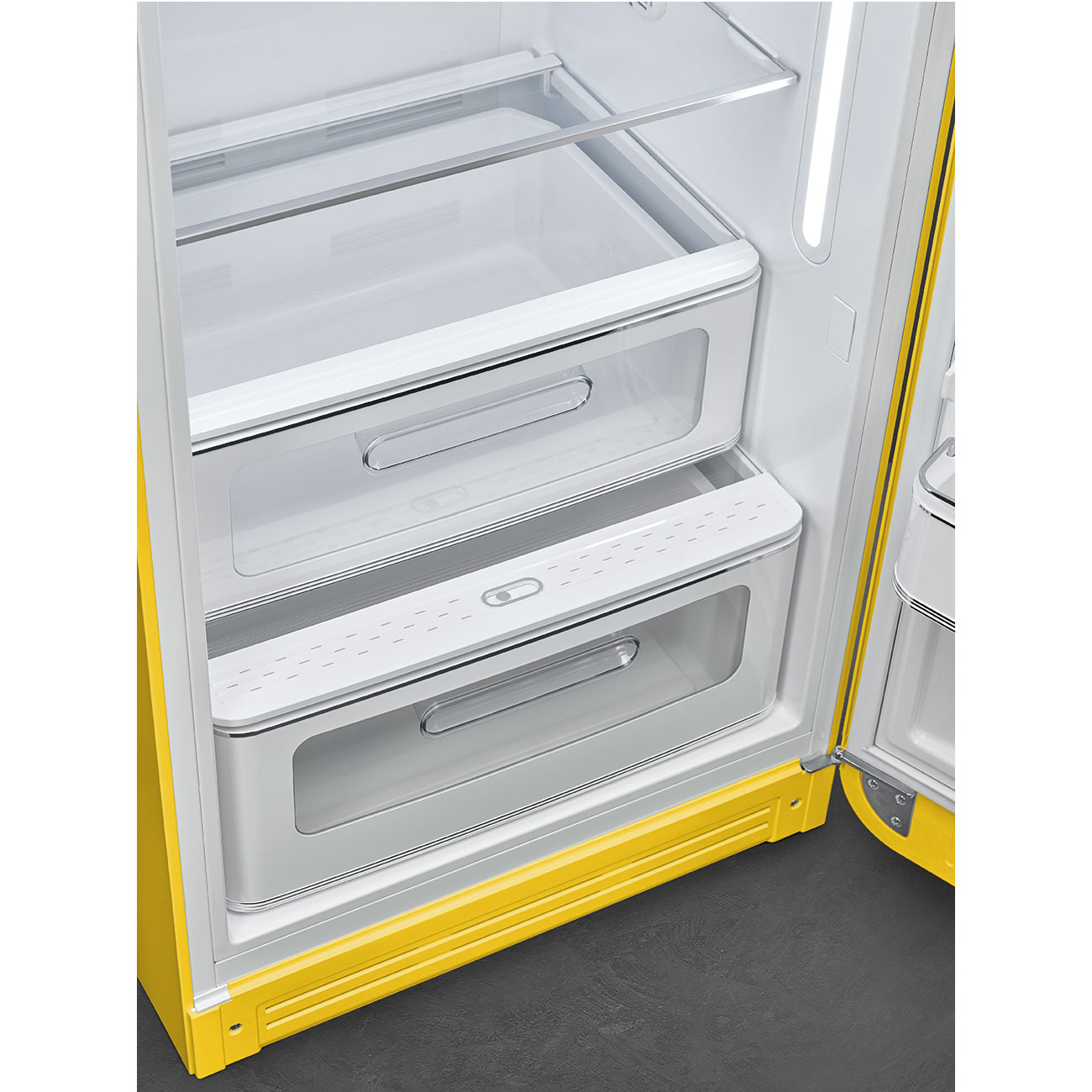 Vista interior de un refrigerador amarillo con la puerta abierta. Muestra cajones y estantes blancos. El interior es brillante.