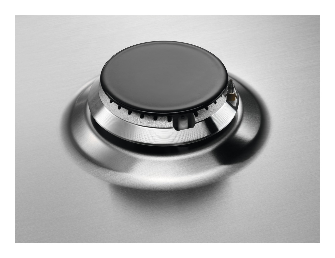 Zbliżenie palnika kuchenki gazowej ze stali nierdzewnej. Palnik ma czarny element centralny i srebrną, okrągłą ramę.