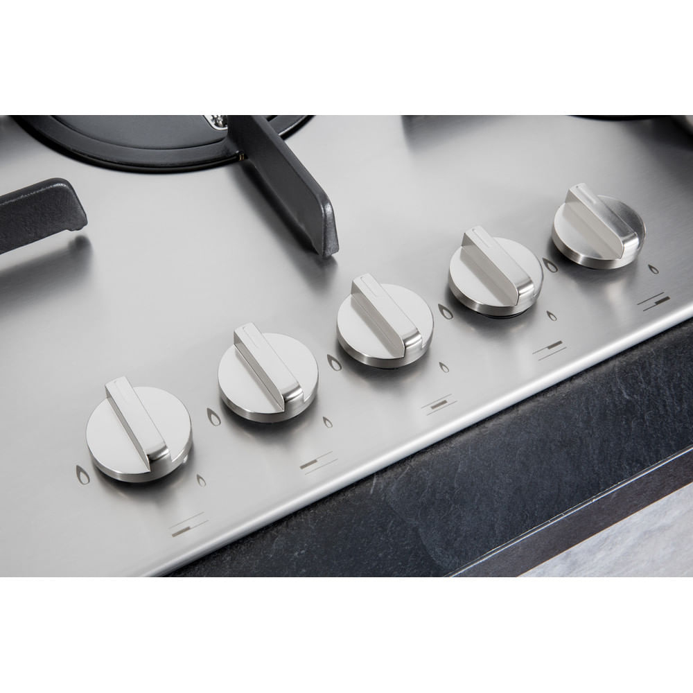 Zbliżenie na stalową płytę grzejną z pięcioma srebrnymi pokrętłami. Kuchenka stoi na czarnym blacie.