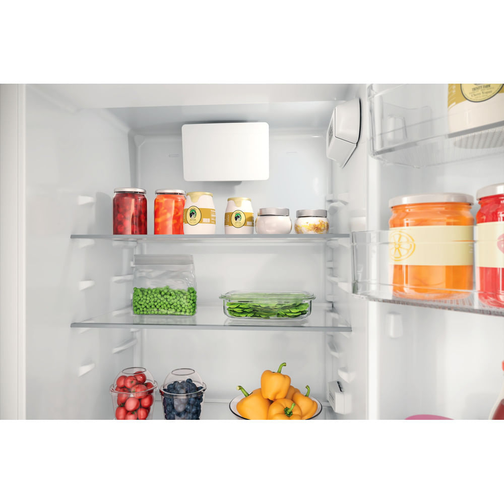 W lodówce na półkach widać słoiki, warzywa i pojemniki z jedzeniem. Żółta papryka stoi na dolnej półce.