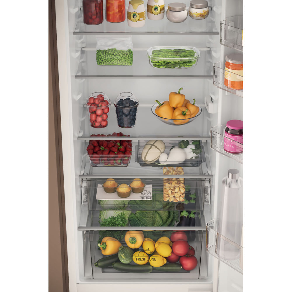 Lodówka wypełniona różnymi produktami spożywczymi: owocami, warzywami, dżemami i pakowanymi produktami, ułożonymi na wielu półkach.