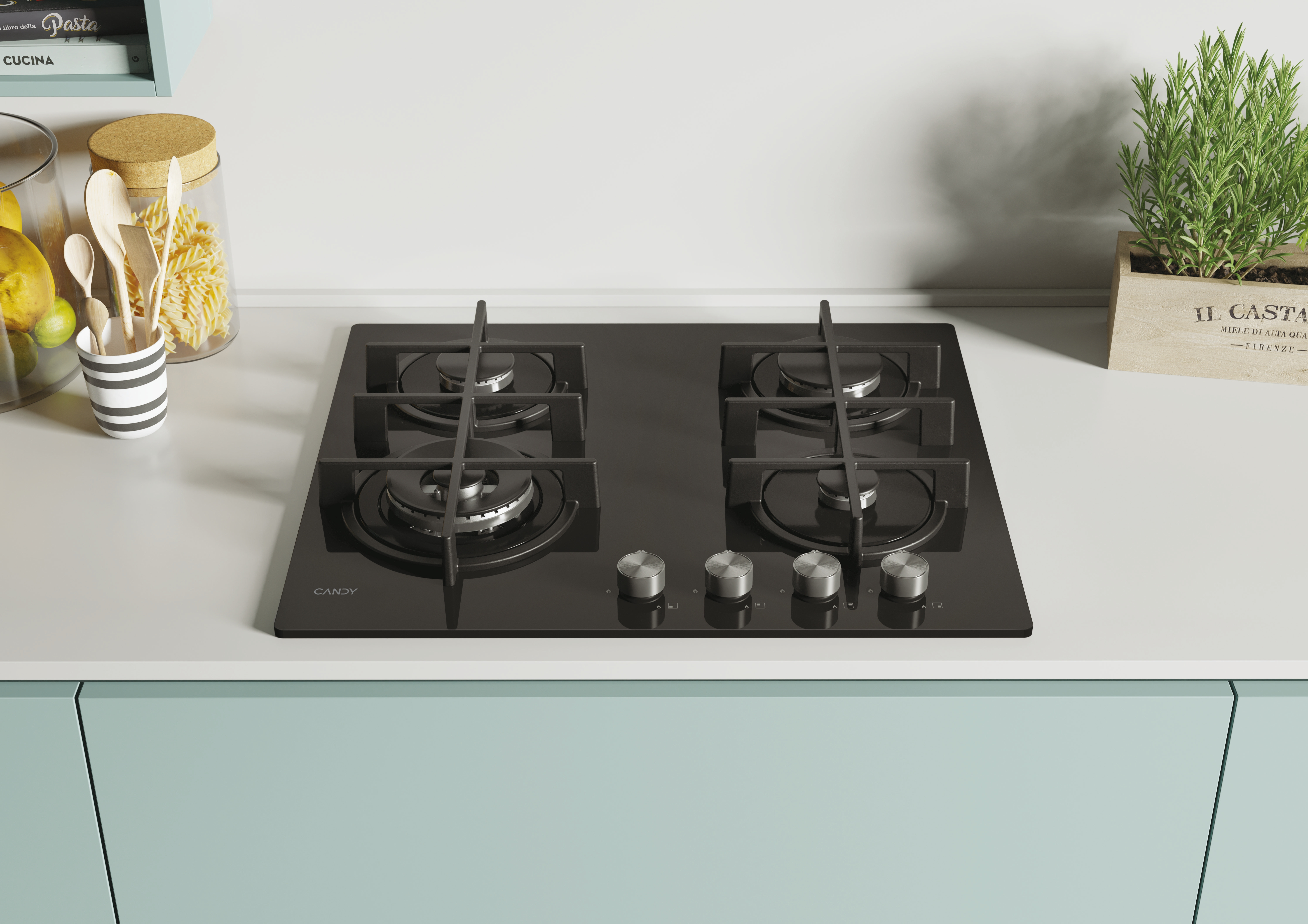 Piano cottura nero con manopole argentate. Barattoli con pasta e limoni, cucchiai di legno e pianta in una scatola di legno.