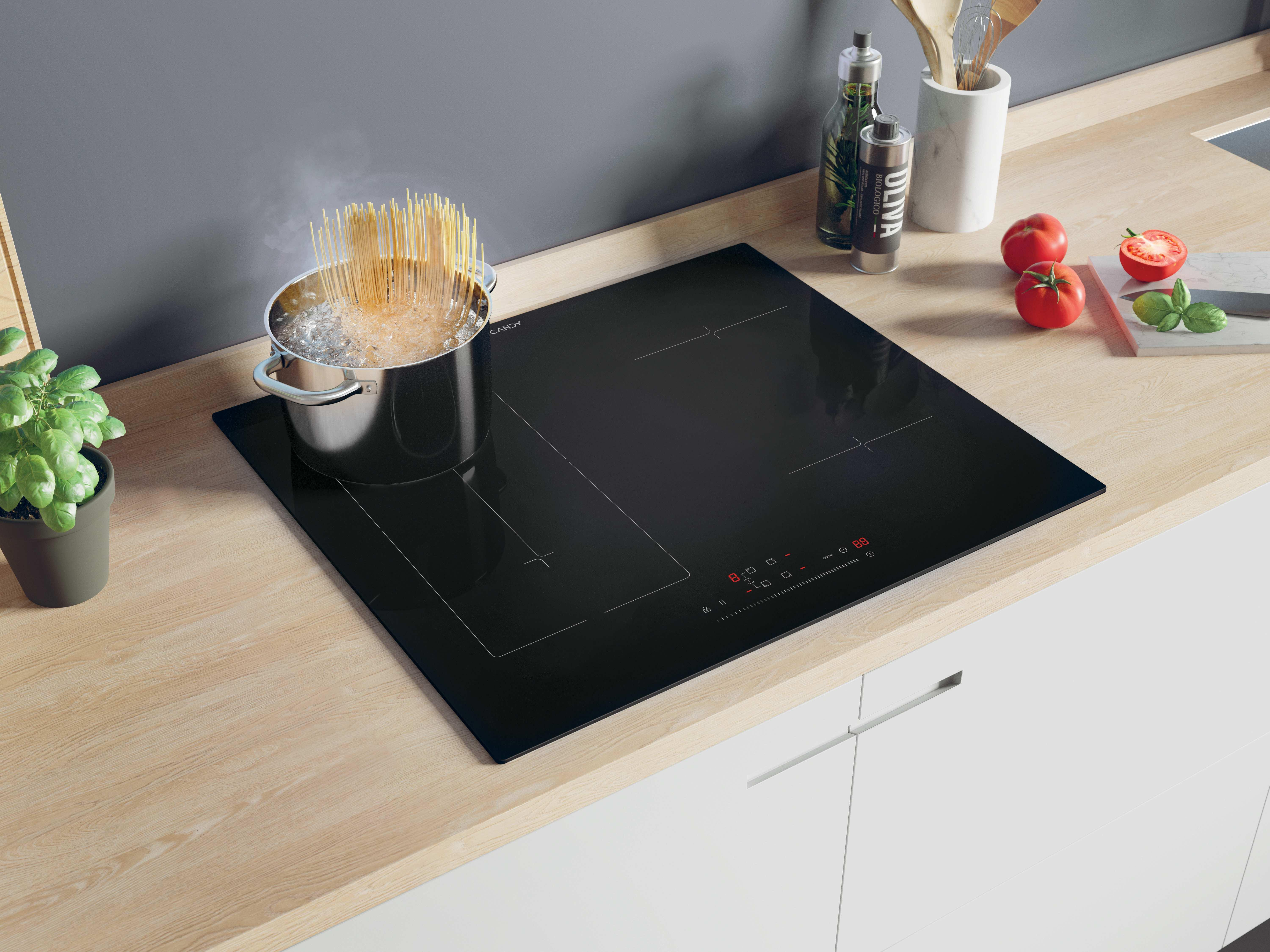 Czarna płyta grzewcza z garnkiem wrzącej wody i makaronem. Pomidory, bazylia i oliwa z oliwek obok.