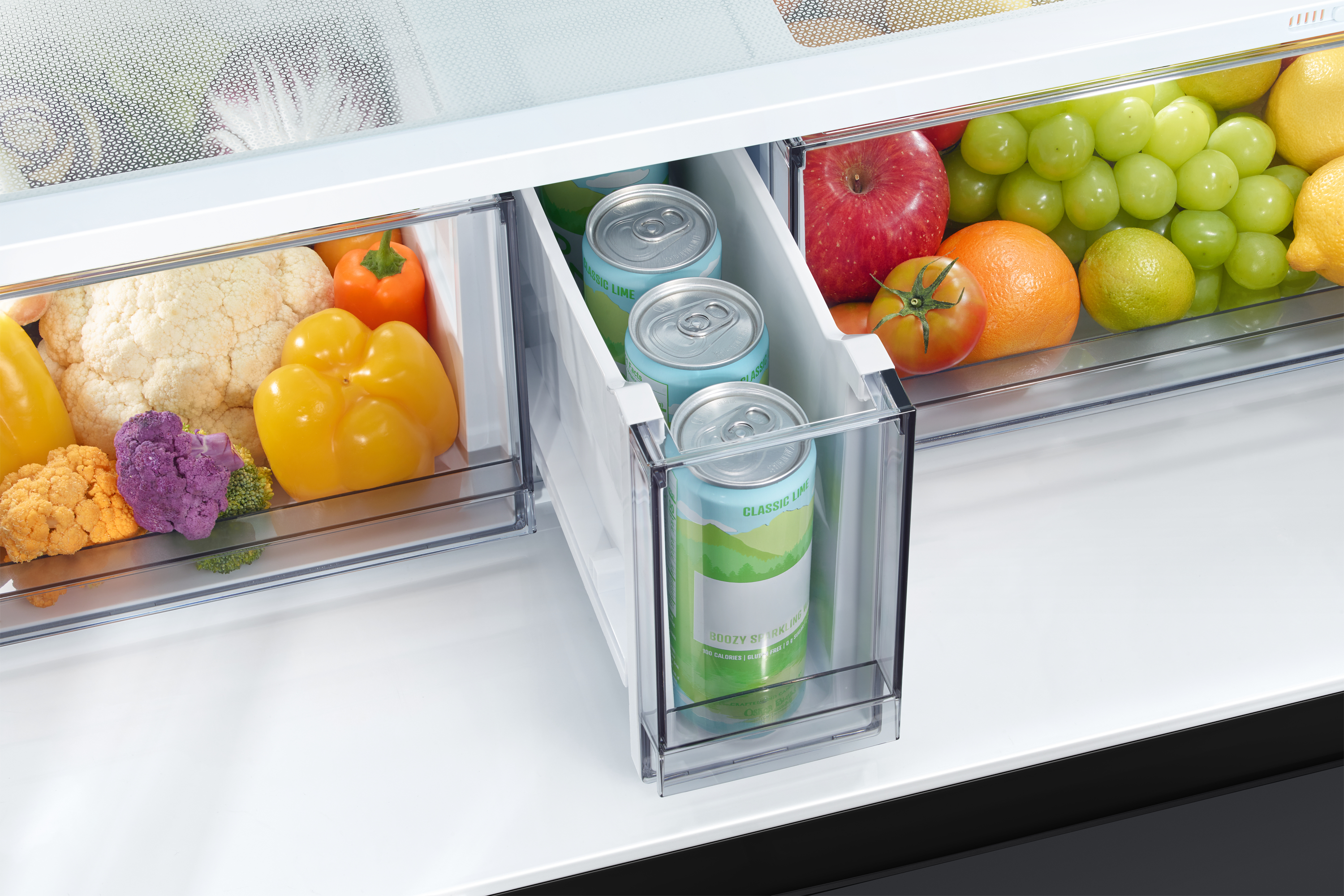Interior de la nevera con verduras, frutas y latas de agua con gas. Incluye coliflor, pimientos, uvas, manzanas y limones.