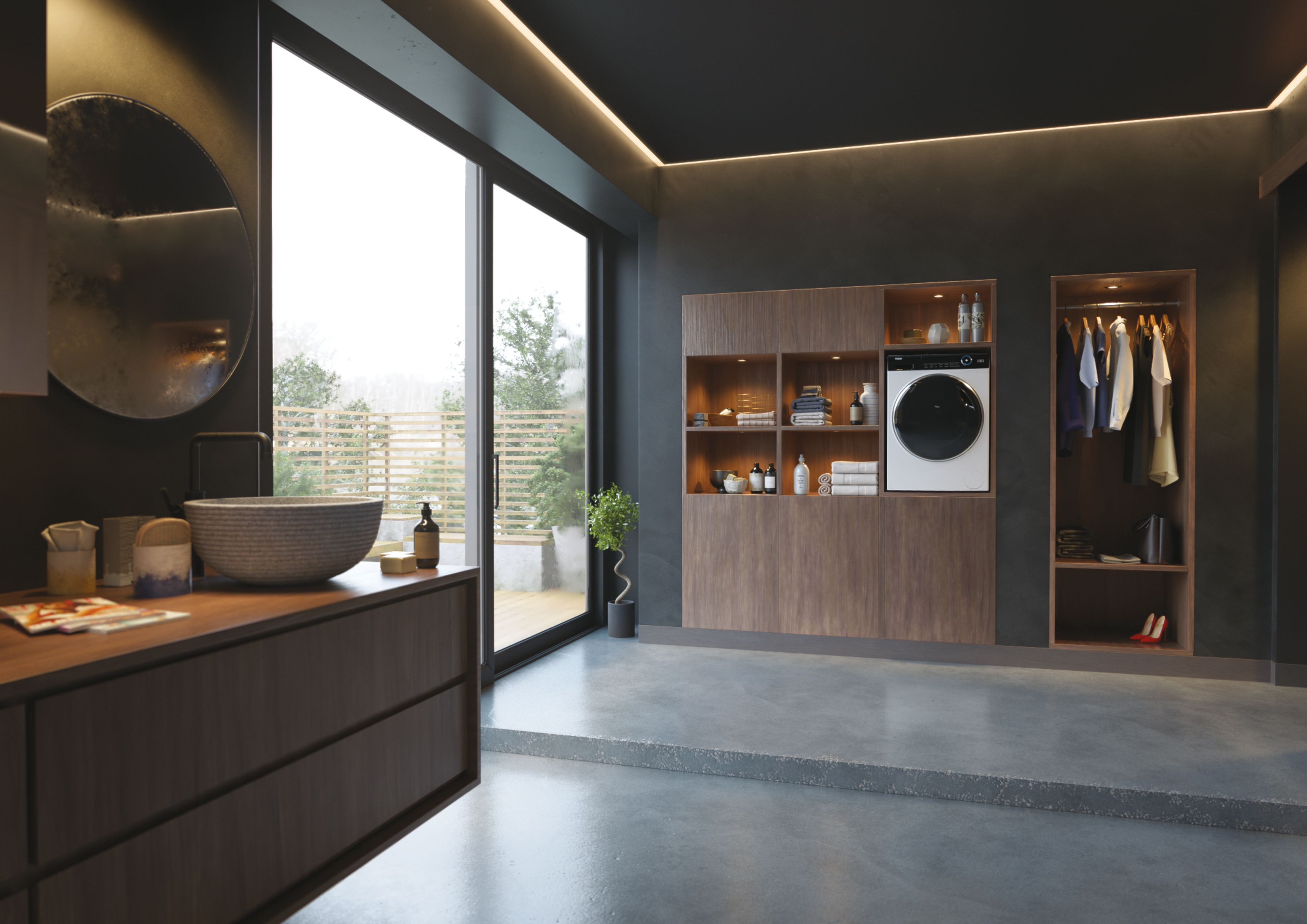 Bagno moderno con lavabo, lavatrice e vestiti. La grande finestra mostra alberi. Mobili in legno scuro e pavimento grigio.